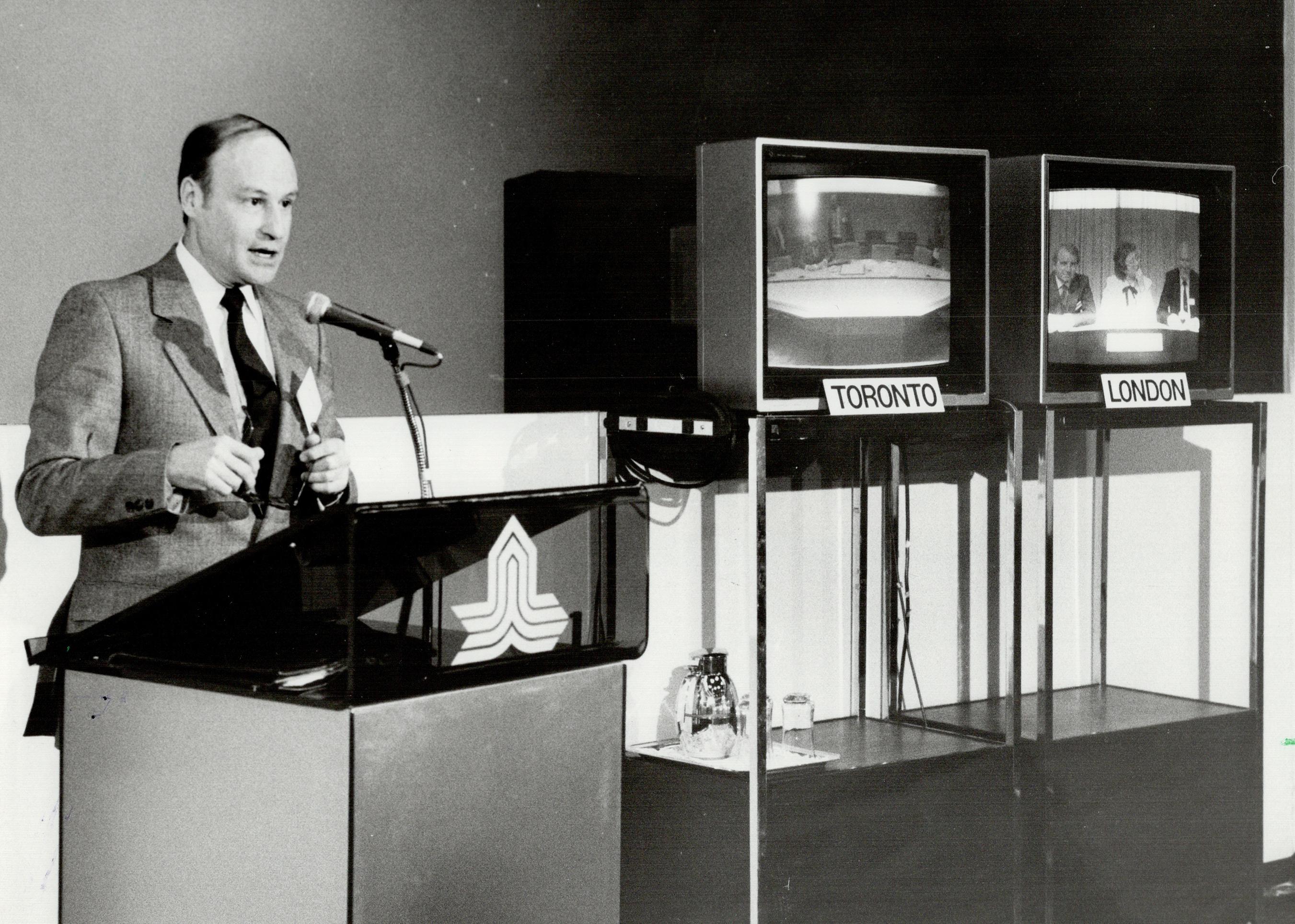 Man speaks about a new trans-Atlantic video-conference service with panelists on television screens