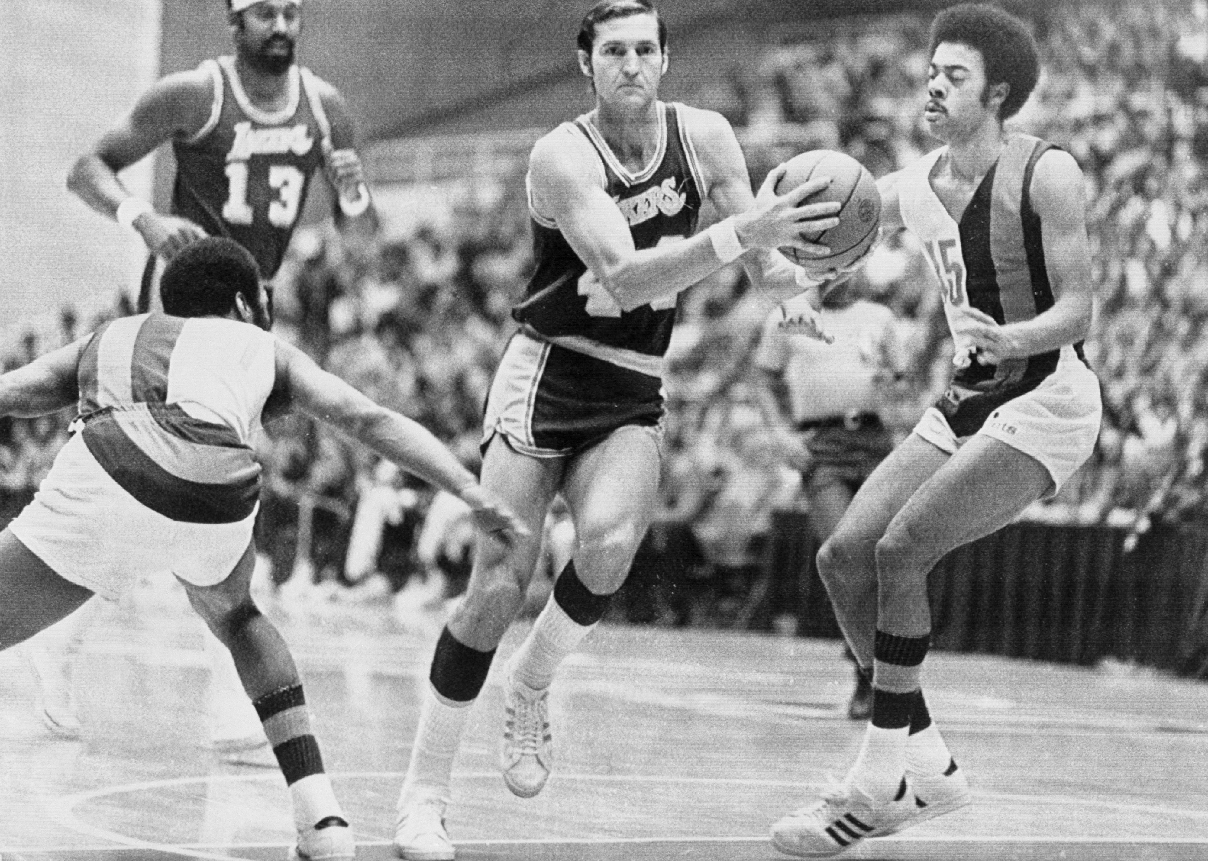 Jerry West drives up the middle of a court with a ball.