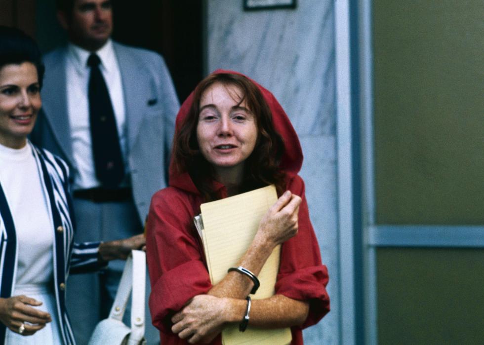 A woman in handcuffs holds a notepad.