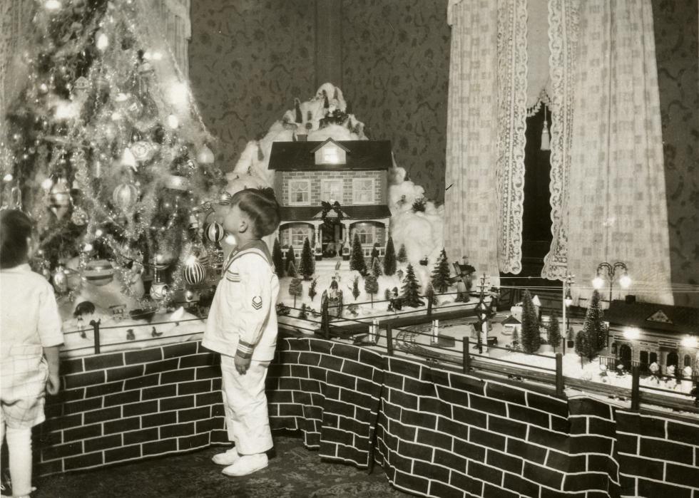 A boy looks up at a Christmas tree decorated with lights.