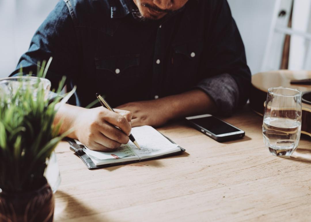 A person in a denim shirt making a checklist at a desk.