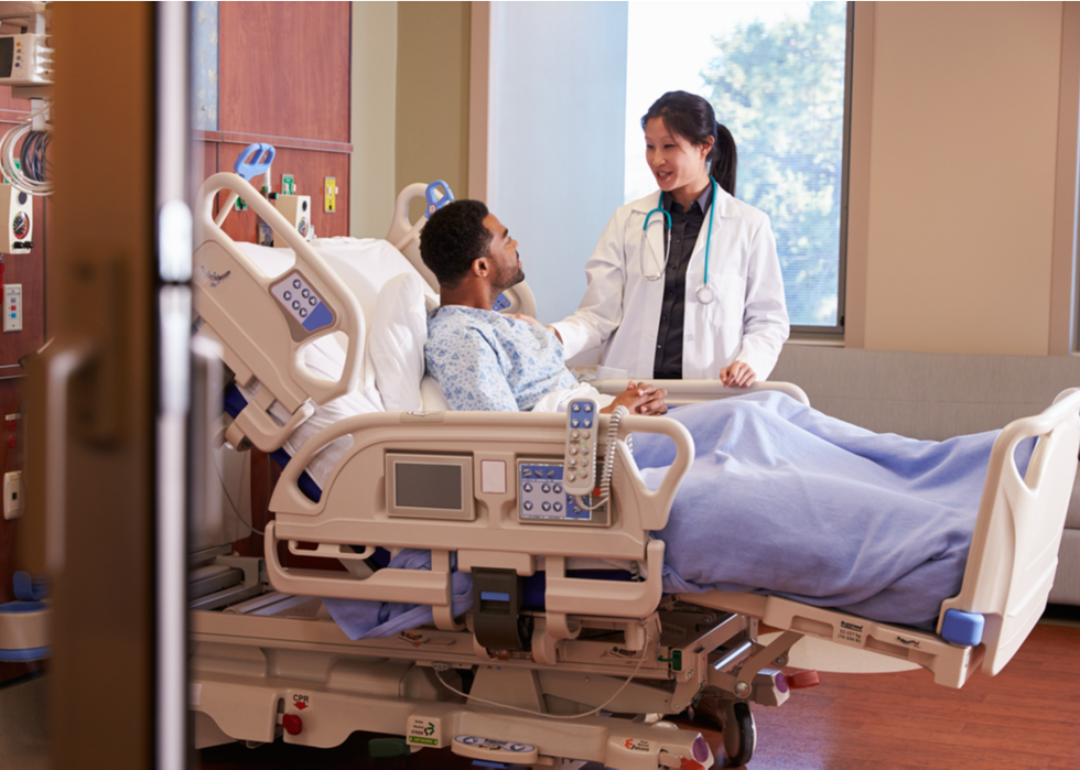 Female doctor talks with a male patient in his hospital bed.