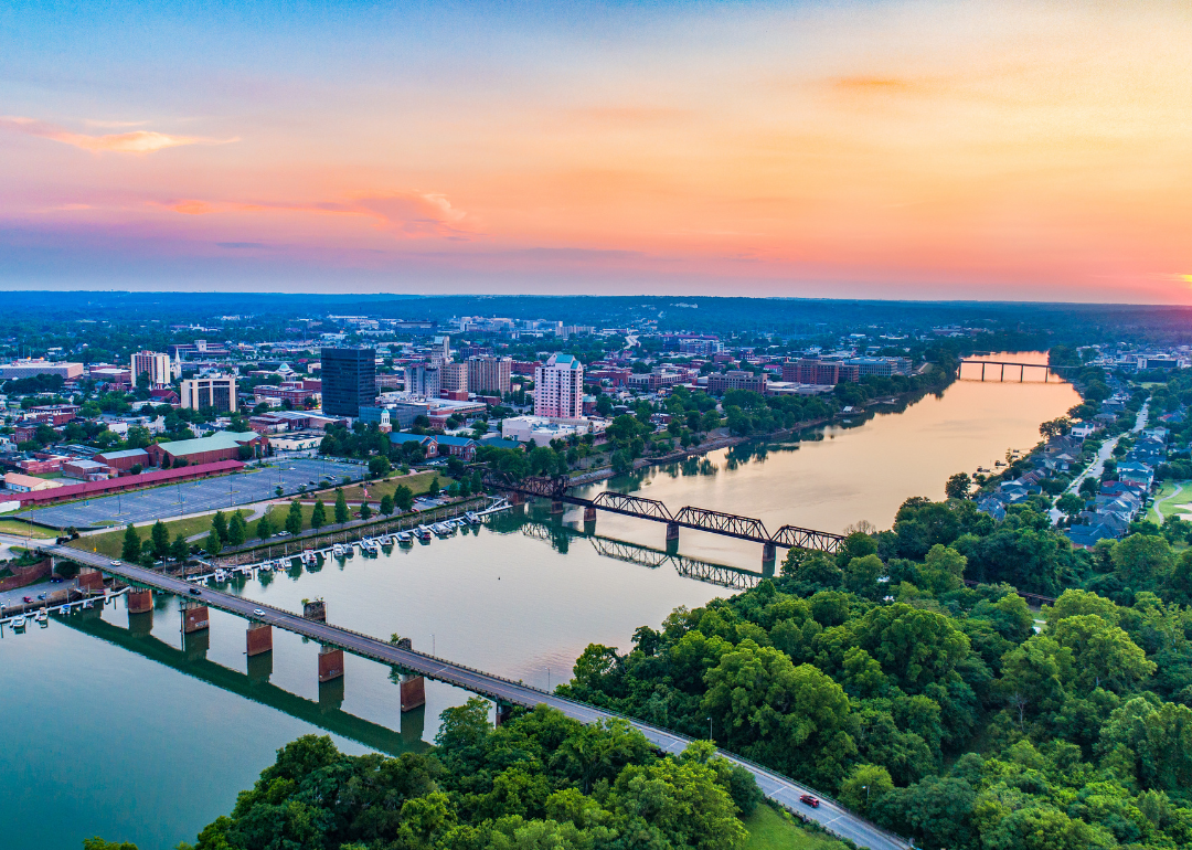 Downtown Augusta, Georgia, with buildings and homes on the water in front of a pink sunset.