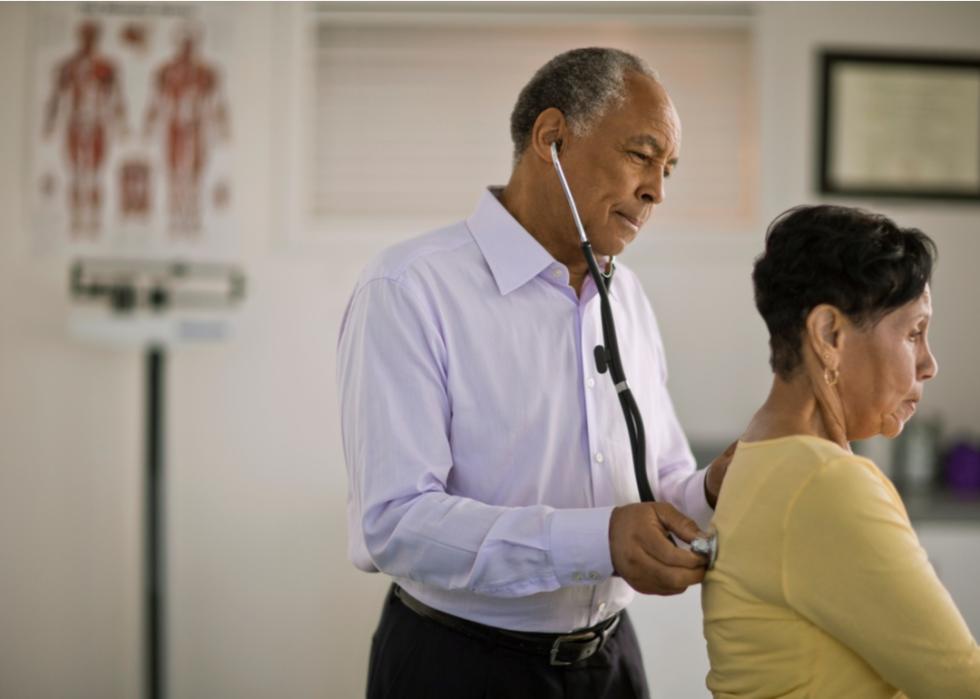 A doctor listens to a patient's lungs using a stethoscope on her back.