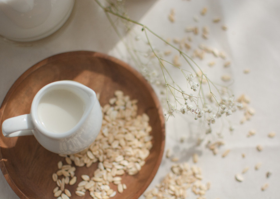 A small jar of oat milk in a wooden tray of oats.