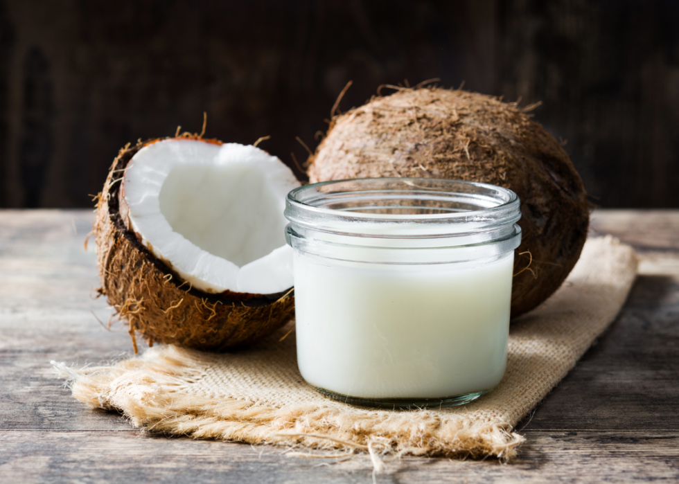 Coconuts sitting next to a jar of coconut milk on a burlap cloth.