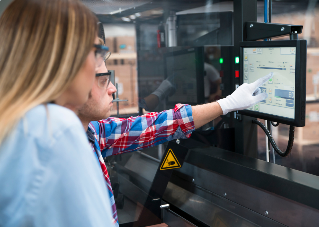 Two people analyzing numbers on a screen at a cable manufacturing plant.