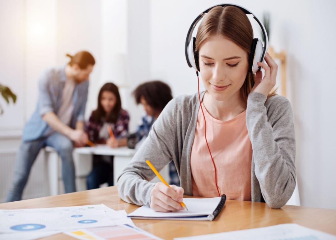 A young woman with red hair listening to headphones with a notebook.