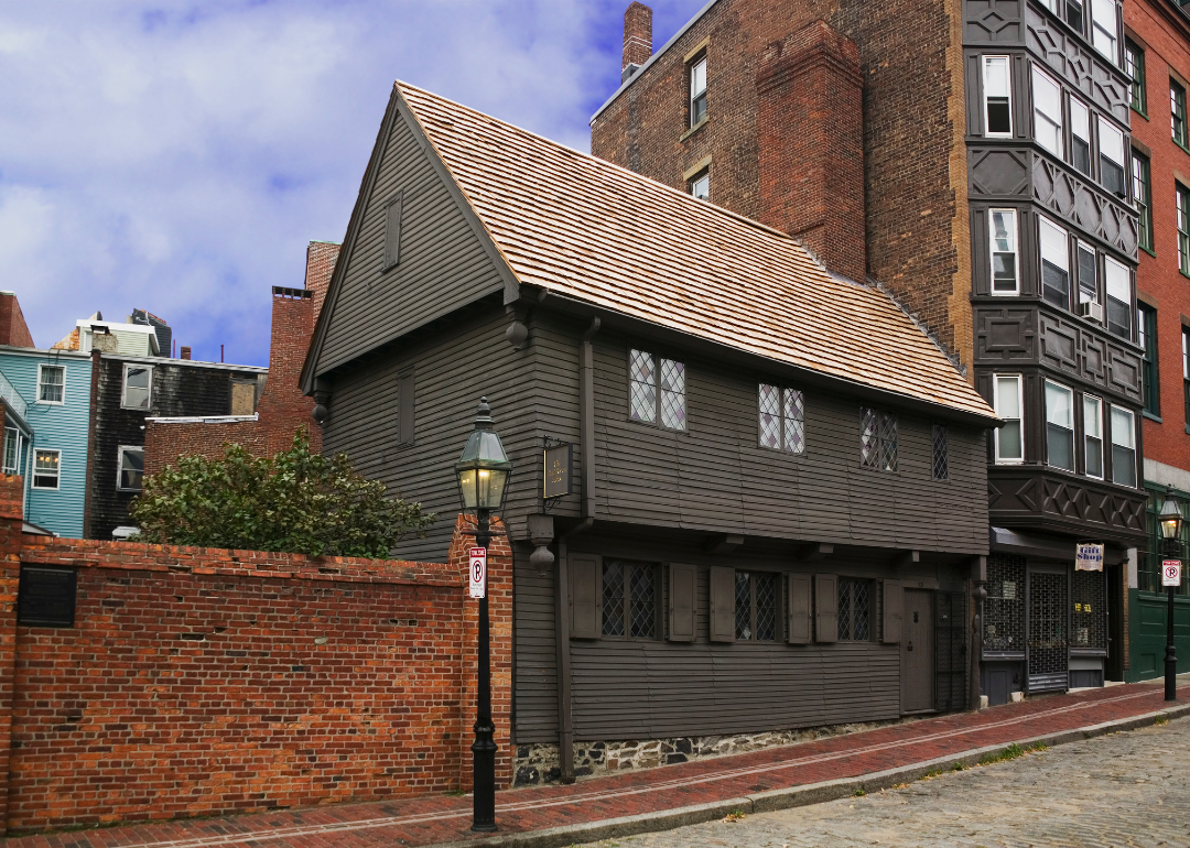 A brown house tucked in between brick buildings on a stone street.