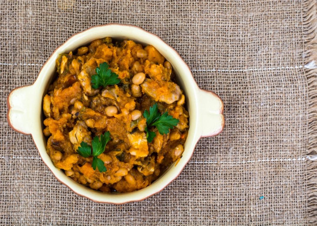 A small crock dish of vegetable and bean cassoulet on a burlap placemat.