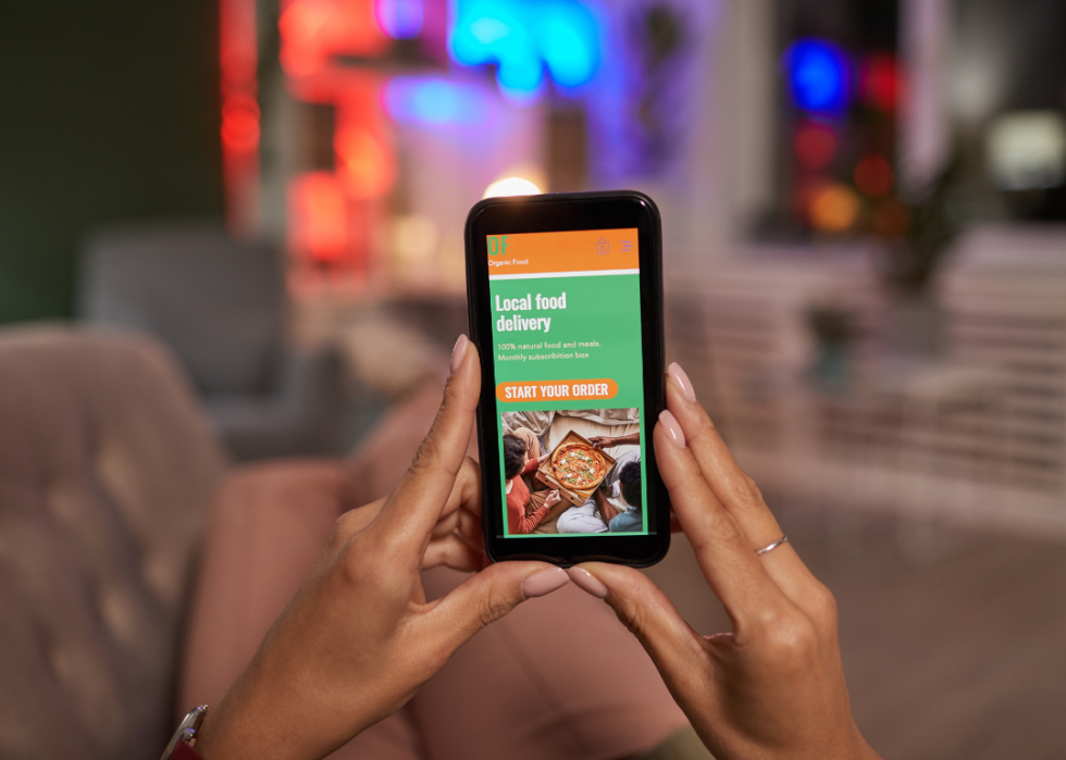 A person holding a phone with a restaurant app open to a pizza delivery.