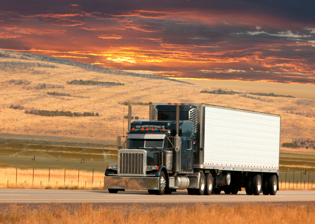 A semi truck driving in front of a beautiful sunset.