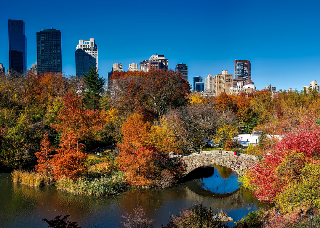 People walking across a stone bridge in Central Park in autumn.
