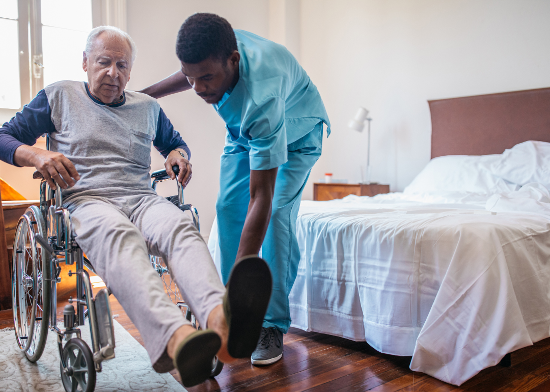 An orderly helping a man in a wheelchair put on shoes.