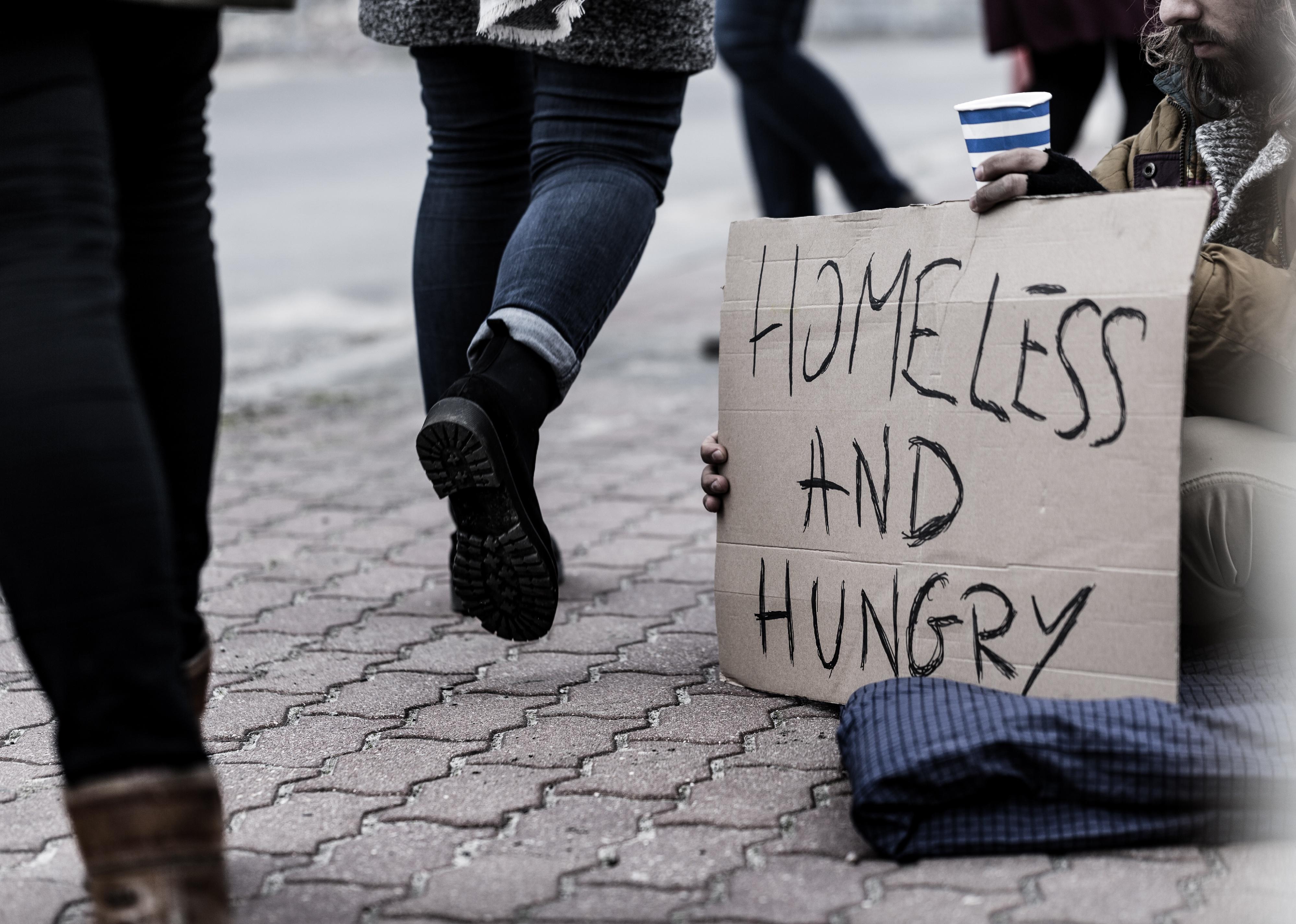 Pedestrians on the sidewalk and homeless man holding a sign.