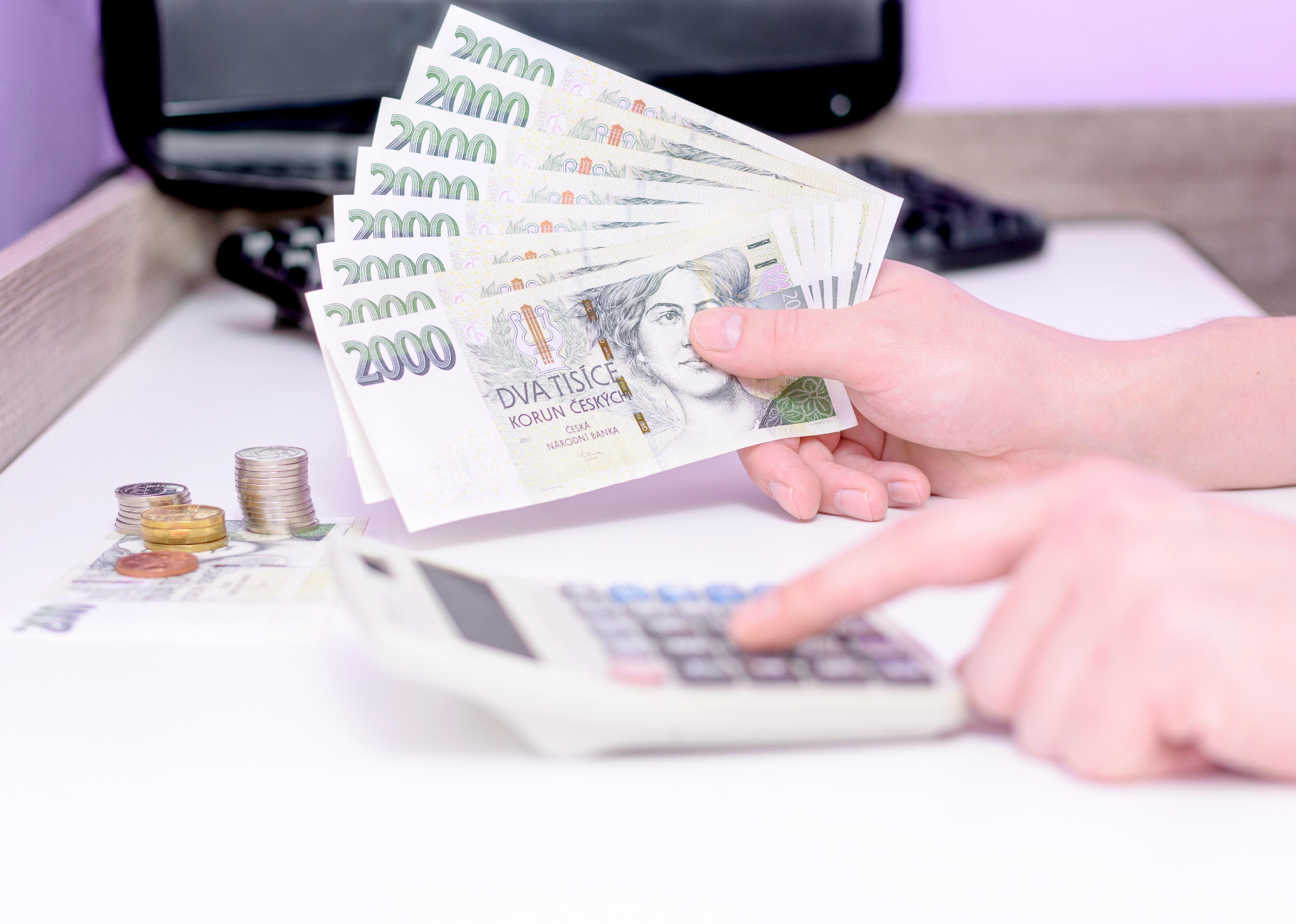 Close-up of hand typing on calculator,  holding a Czech banknotes.