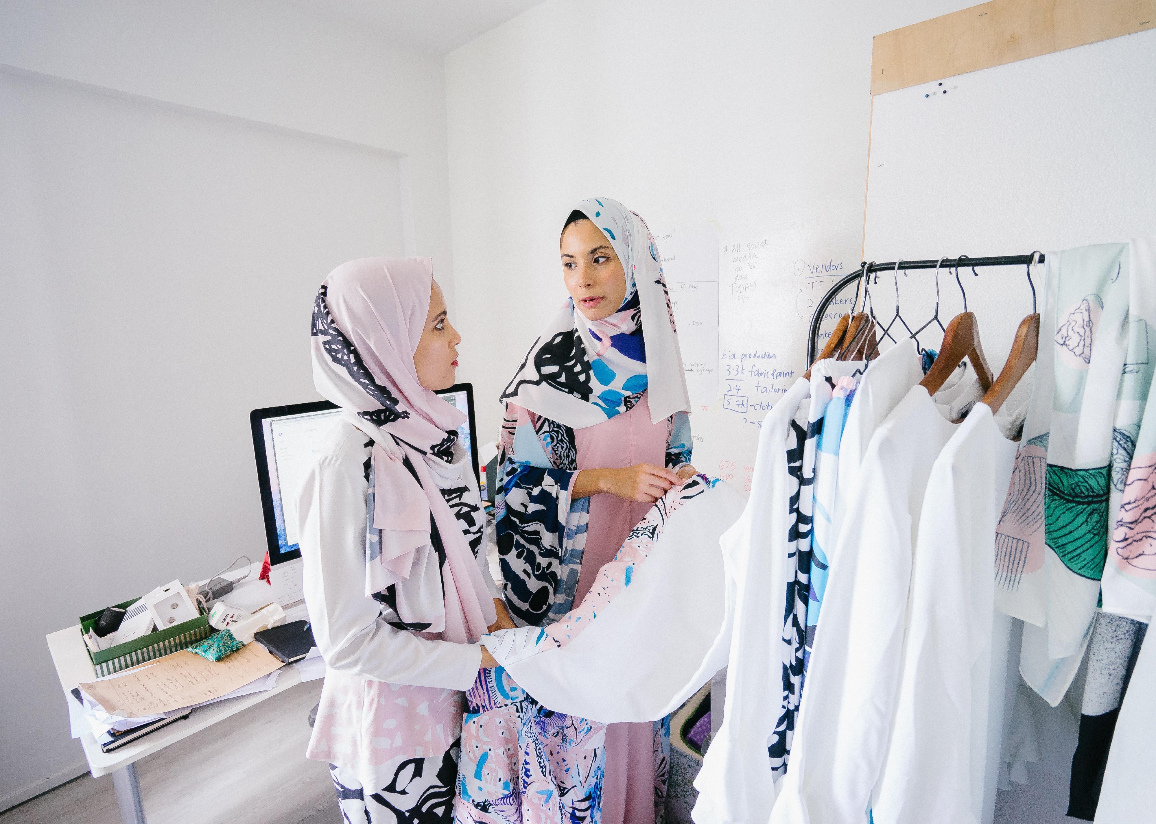 Two people chatting by retail clothing rack.
