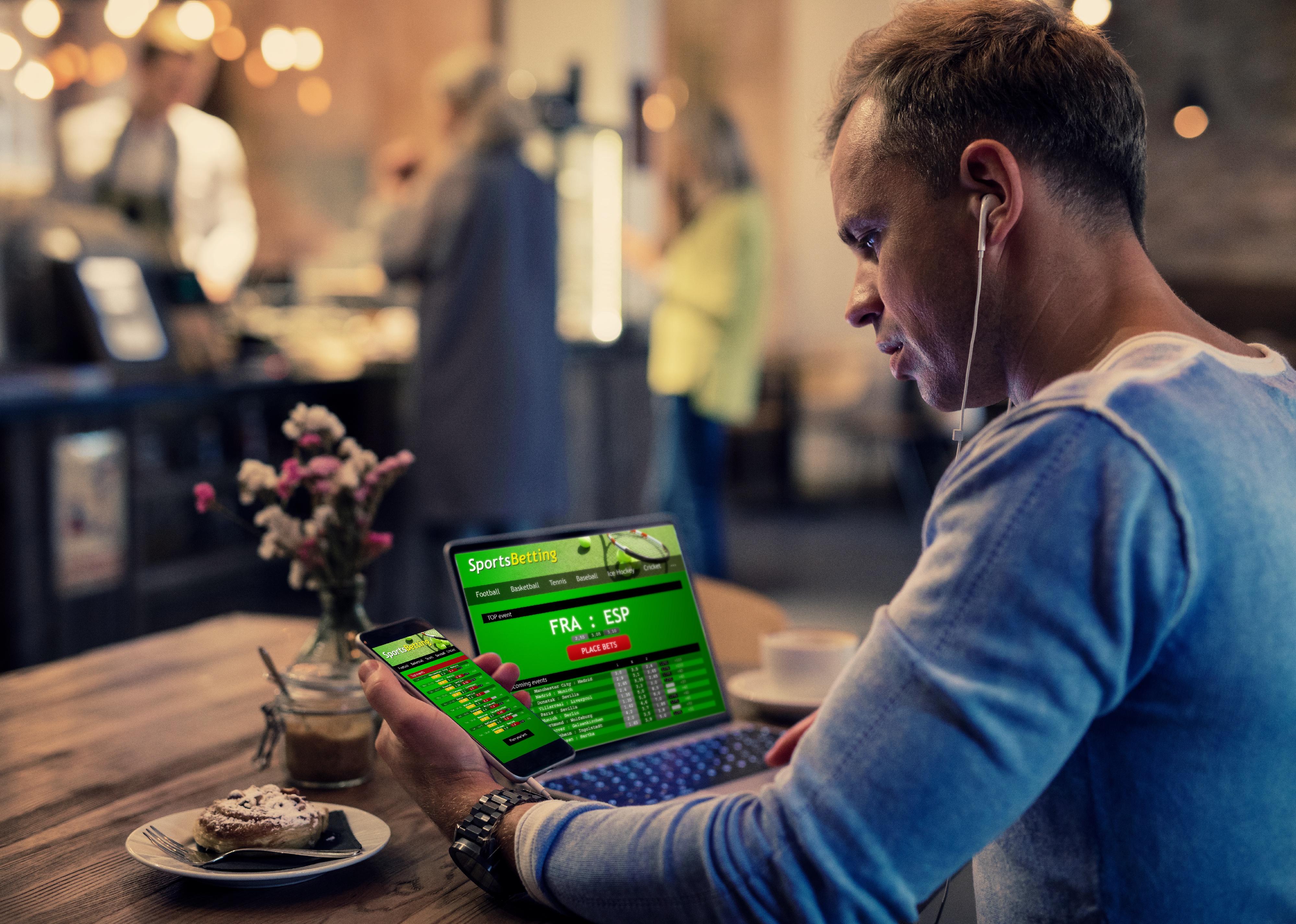 Man using online sports betting services on phone and laptop.