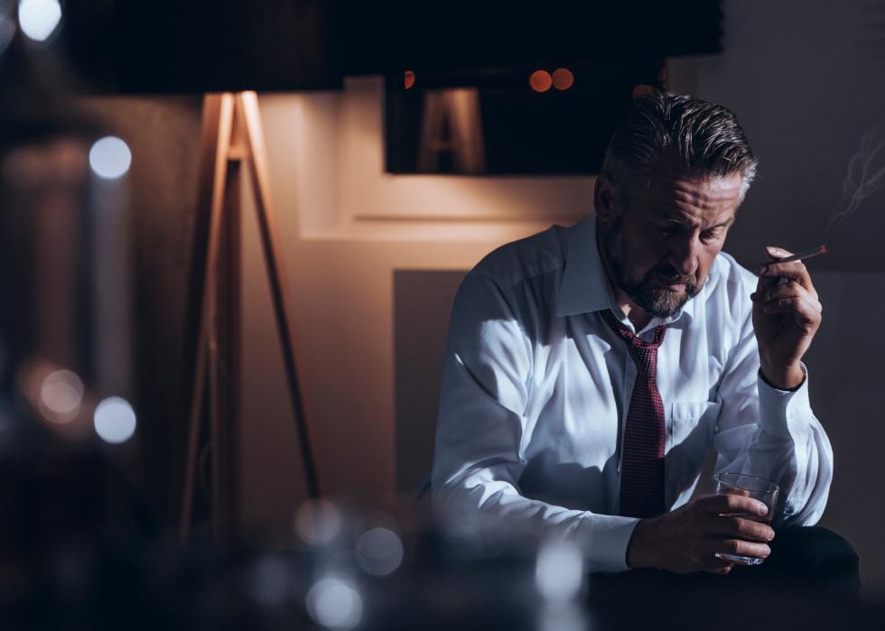 Man smoking a cigarette and drinking alcohol in a dark room
