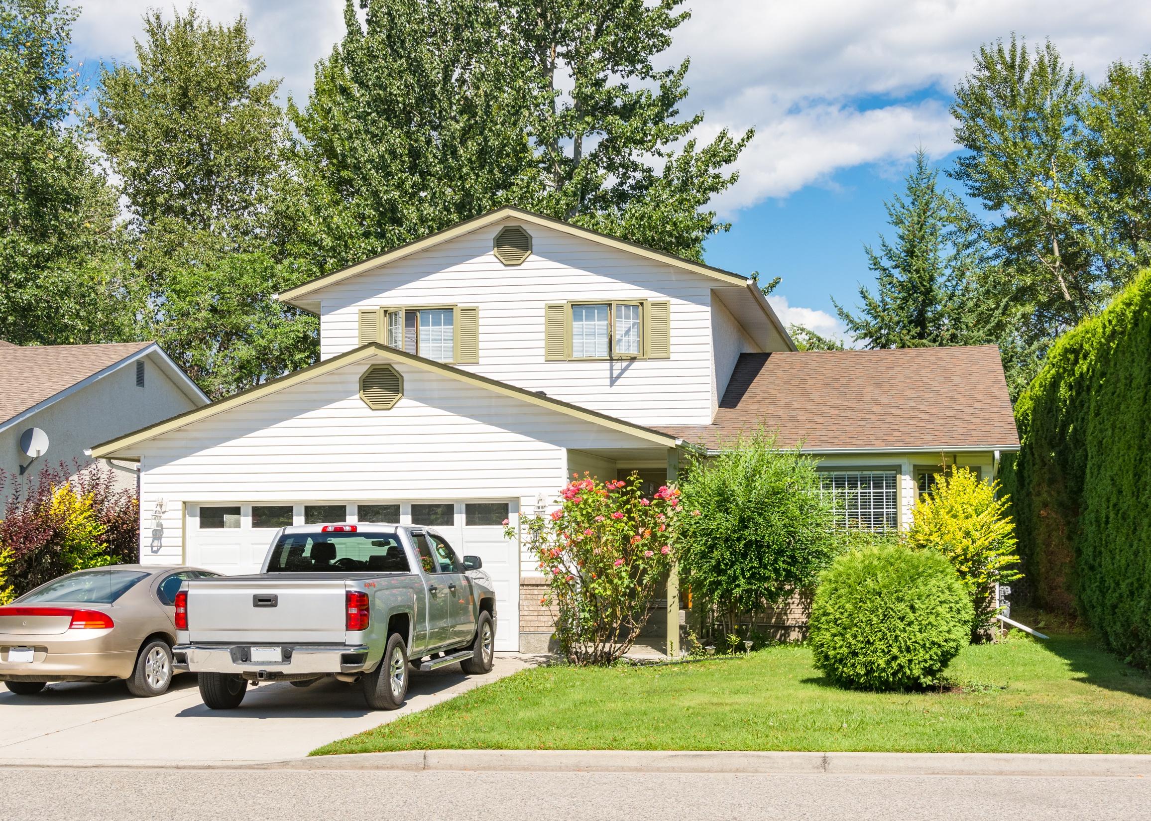 Main entrance of residential house with car and truck parked on concrete driveway in front.
