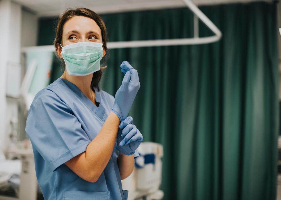 Female nurse with a mask putting on gloves.