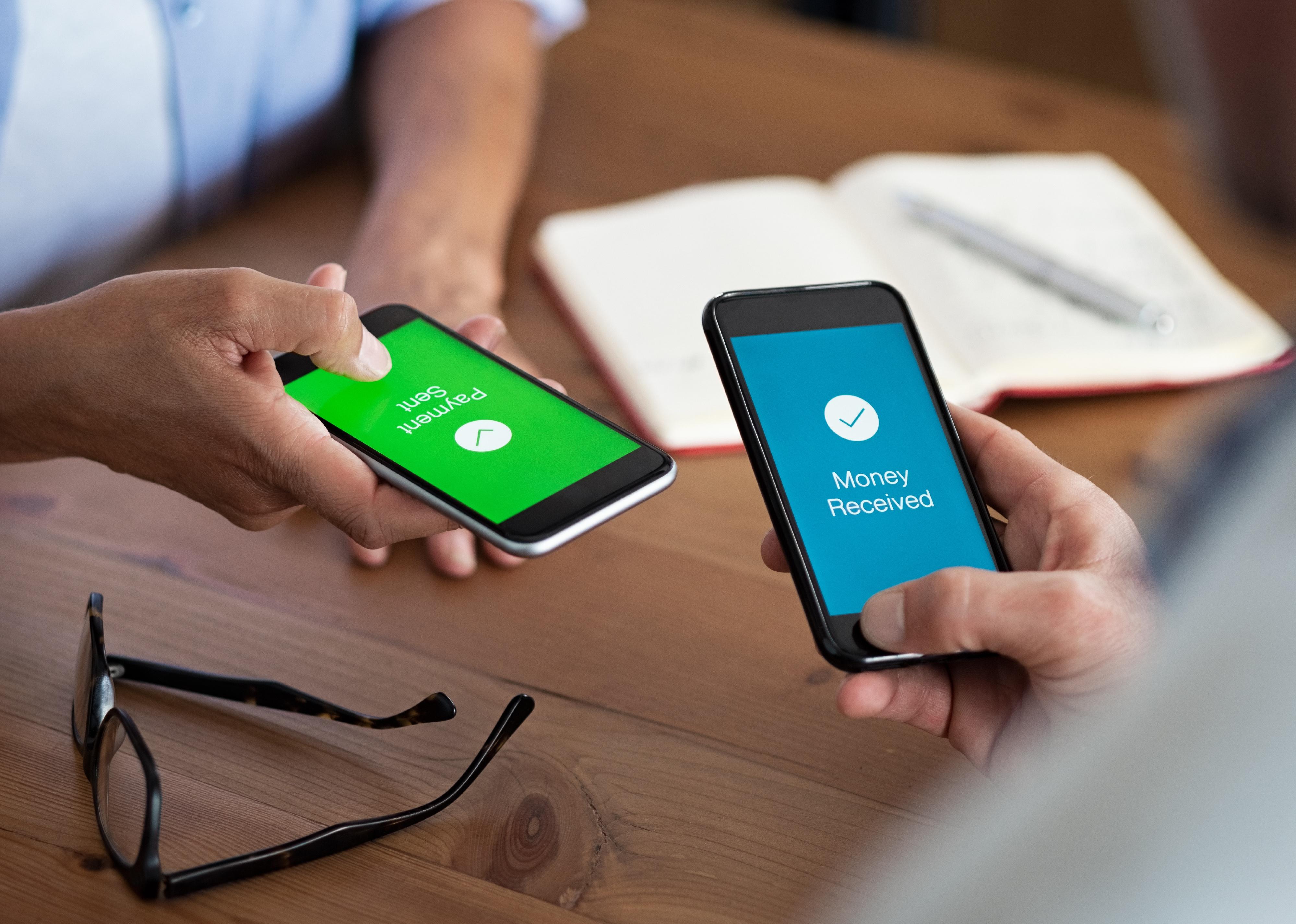 Close-up of two hands holding mobile phones showing money applications