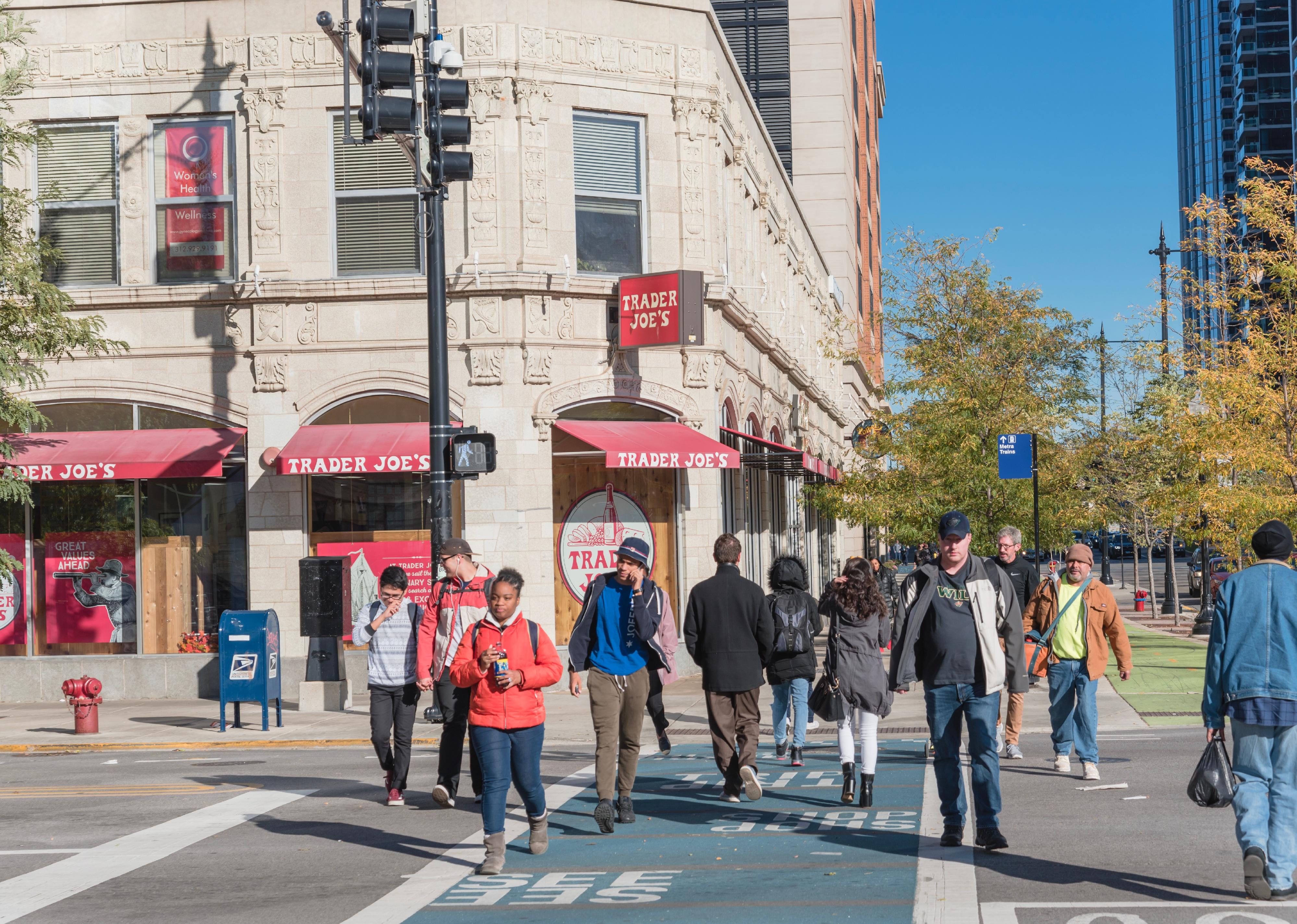 A crowd of pedestrians walking past a supermarket storefront in downtown intersection.