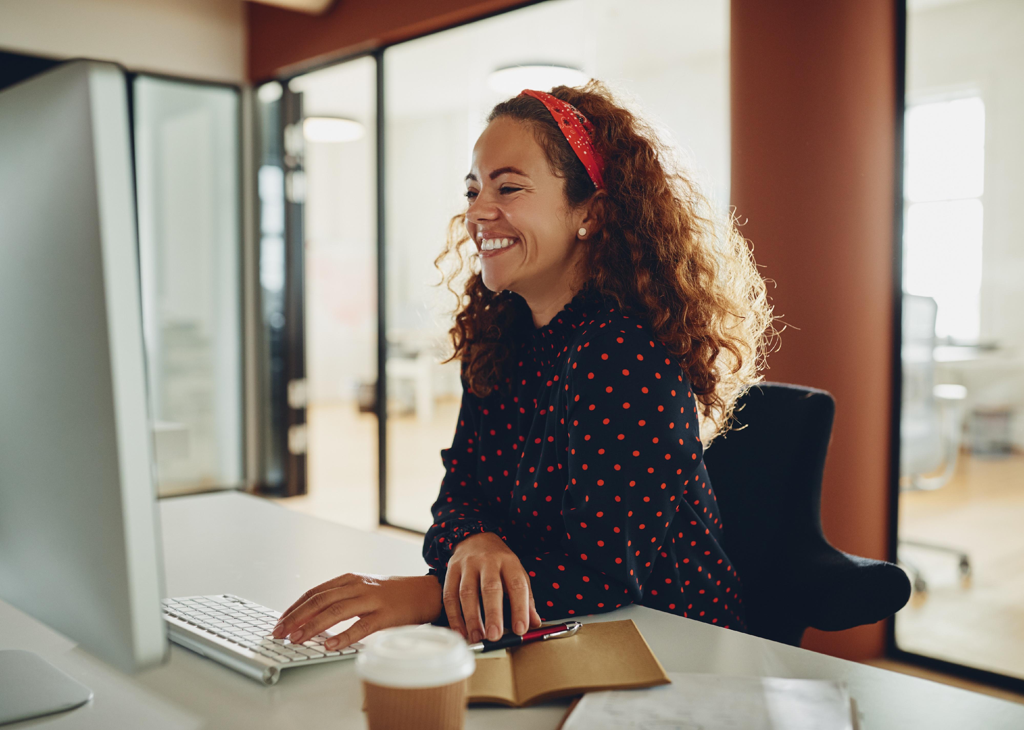 Young sitting at a desk and laughingwhile working on a computer.