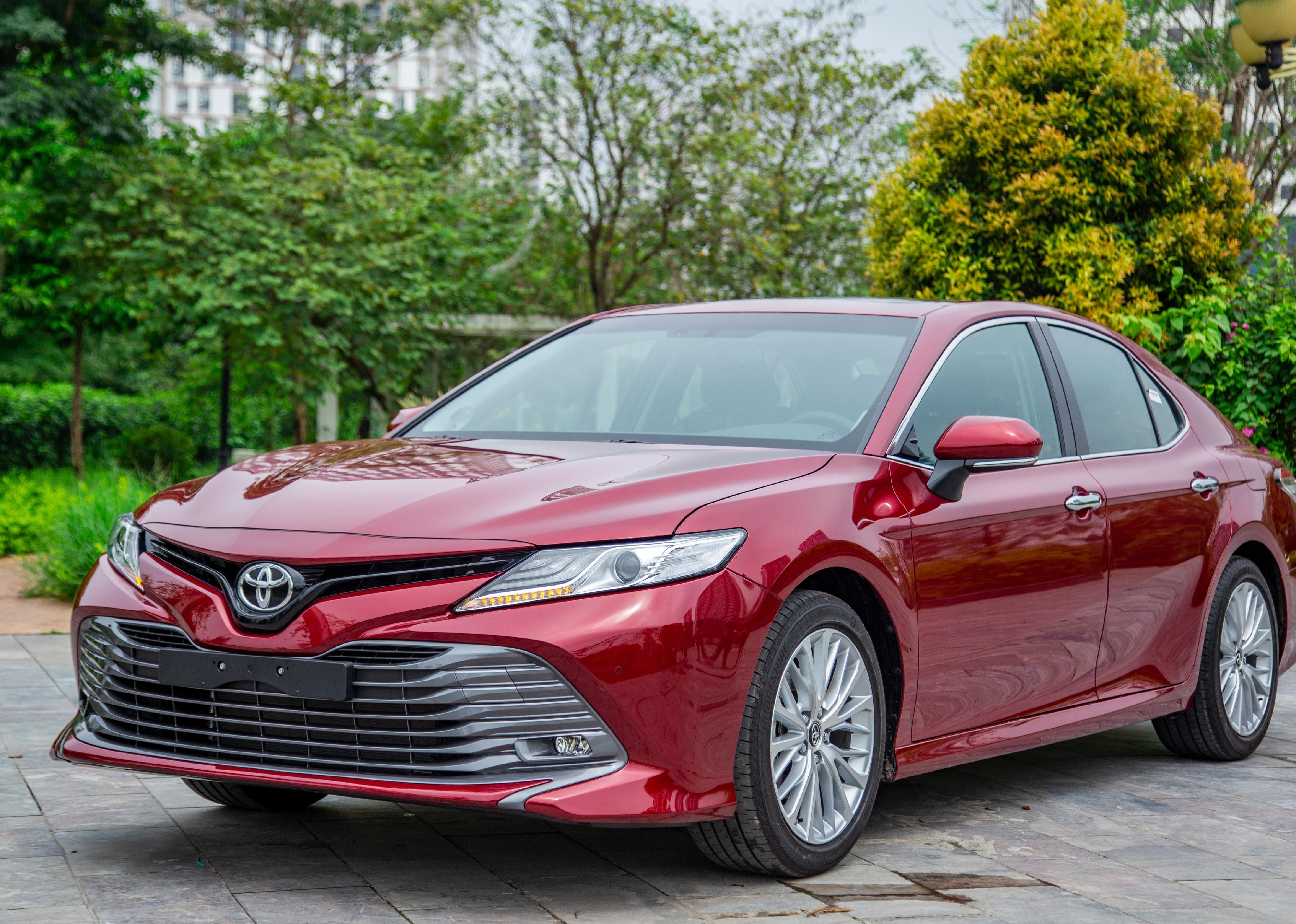 Red Toyota Camry in front of trees.