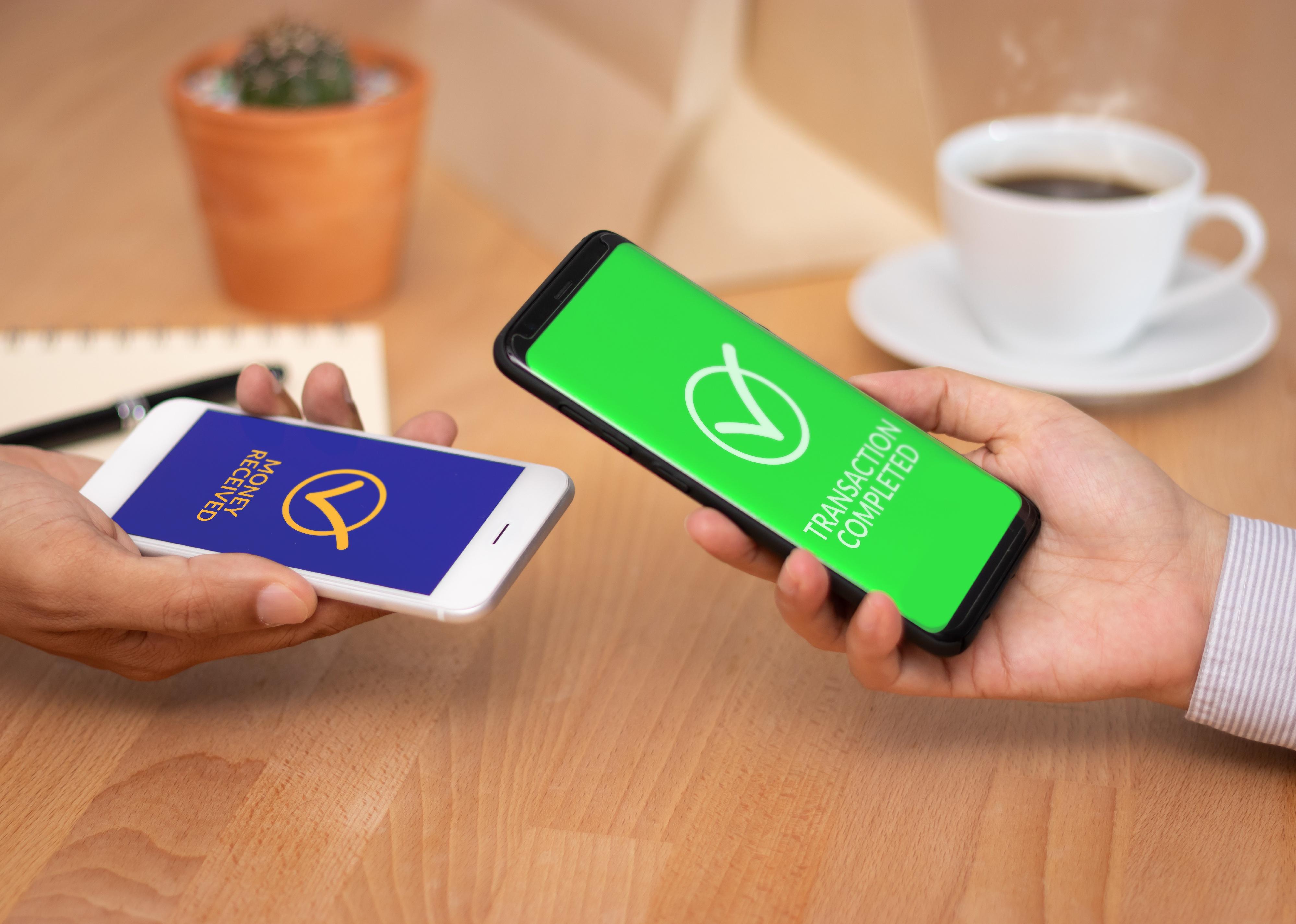 Close-up of two hands holding mobile phones showing money apps