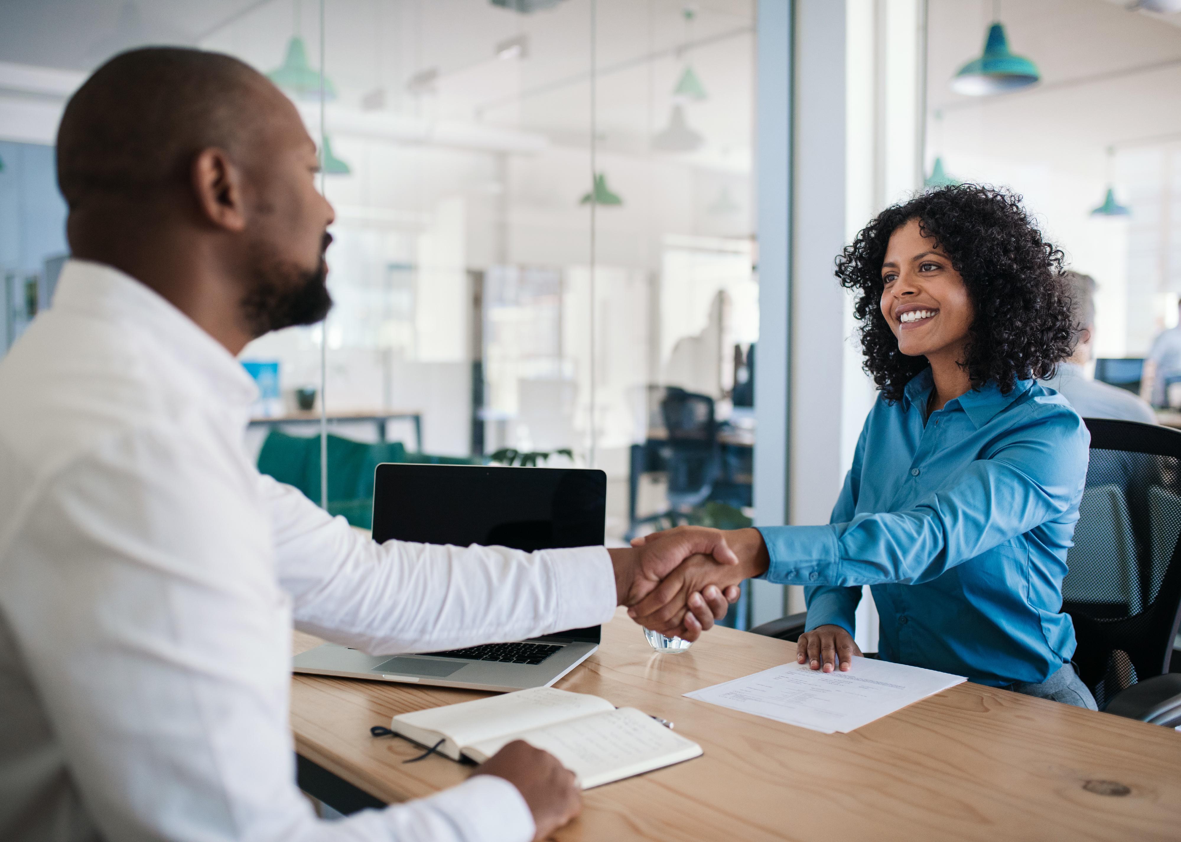 Smiling man sitting at desk shaking hands with a job applicant