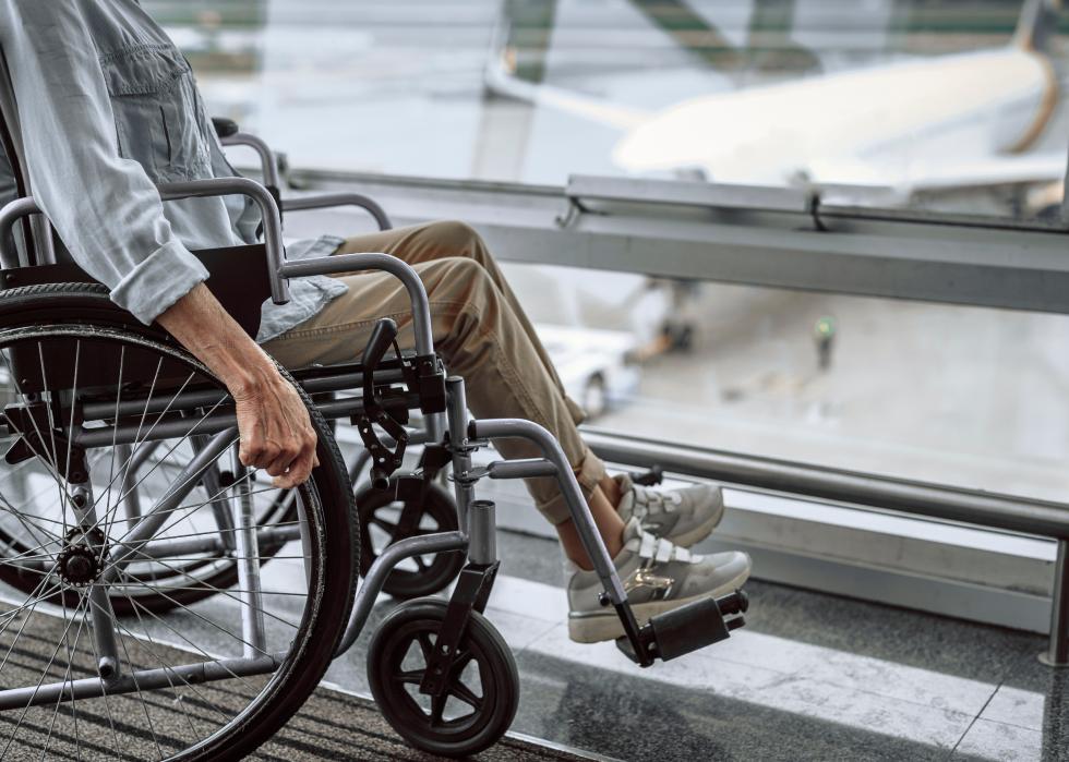 Mature lady on wheelchair waiting in airport hall with airplane in the background