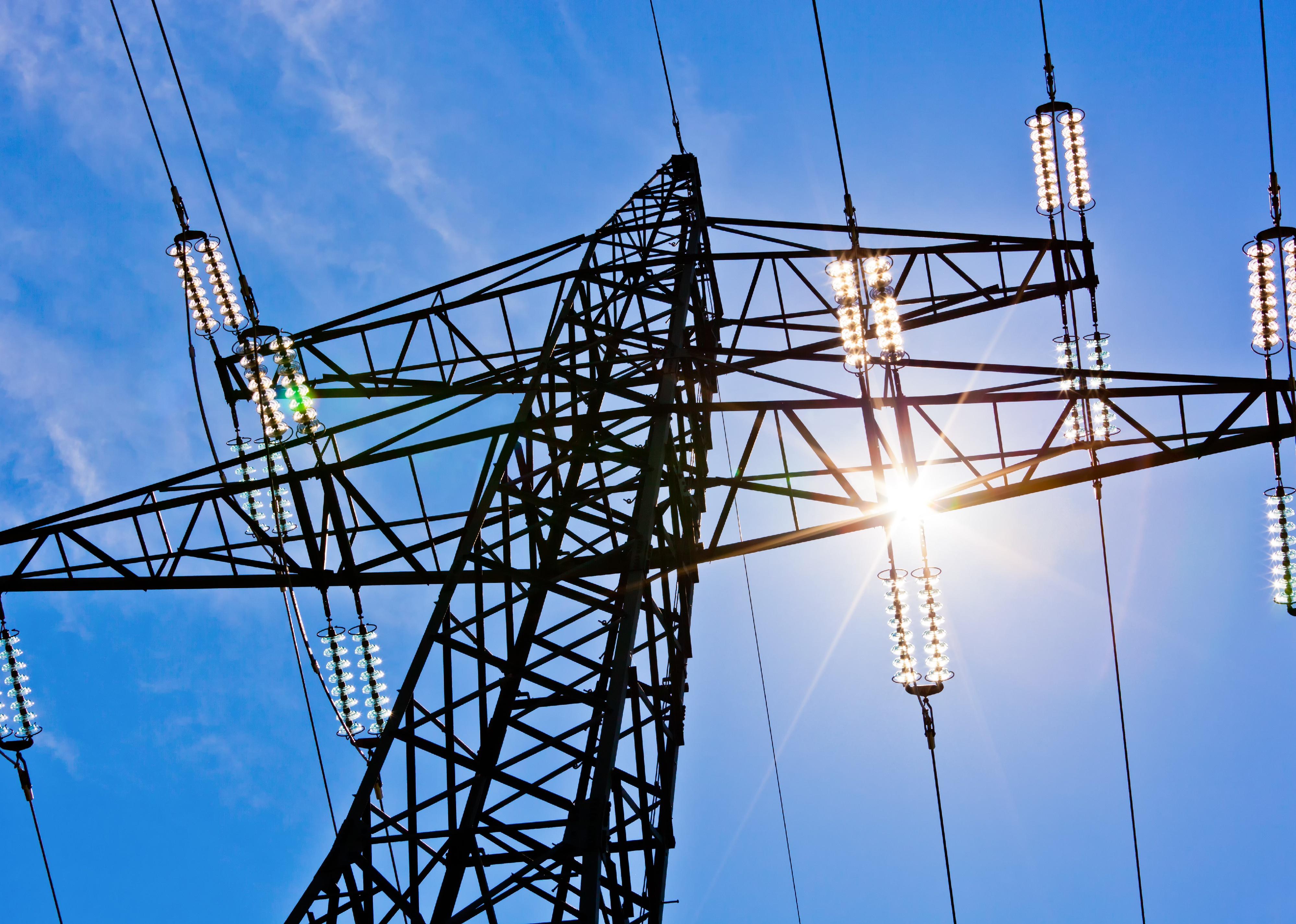 A high voltage power pylons against blue sky and sun rays.