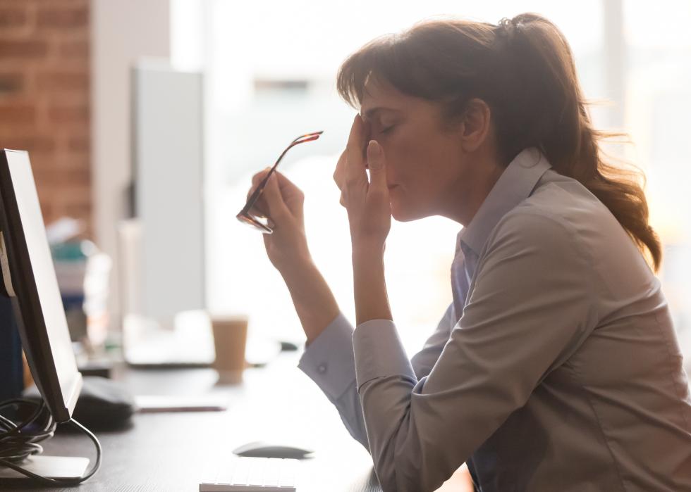 Female worker at office desk takes off glasses