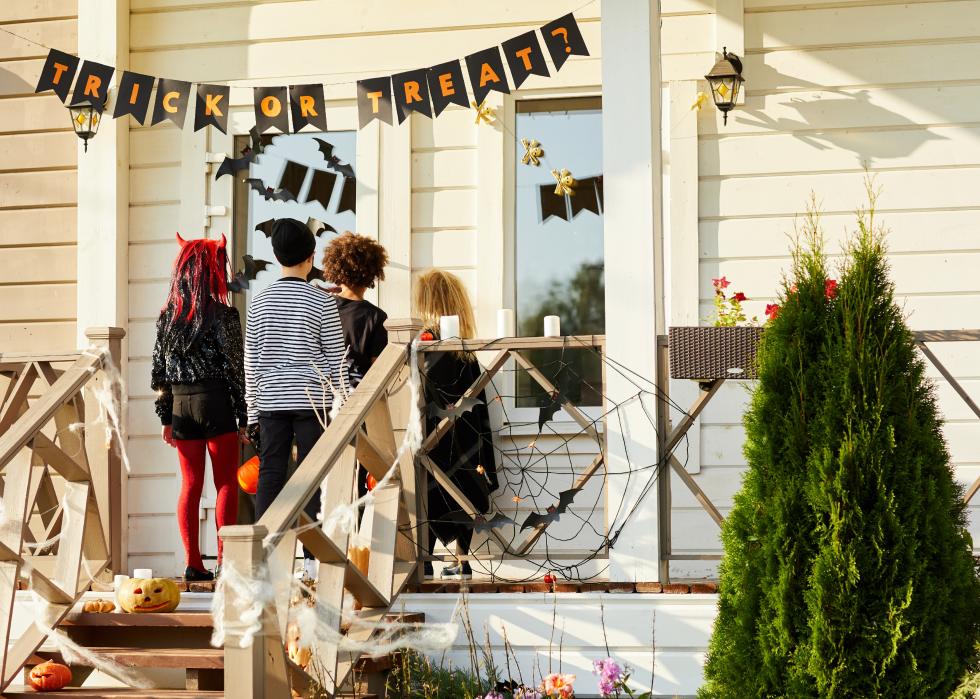View from behind of children waiting at someone's front door, trick or treating on Halloween.