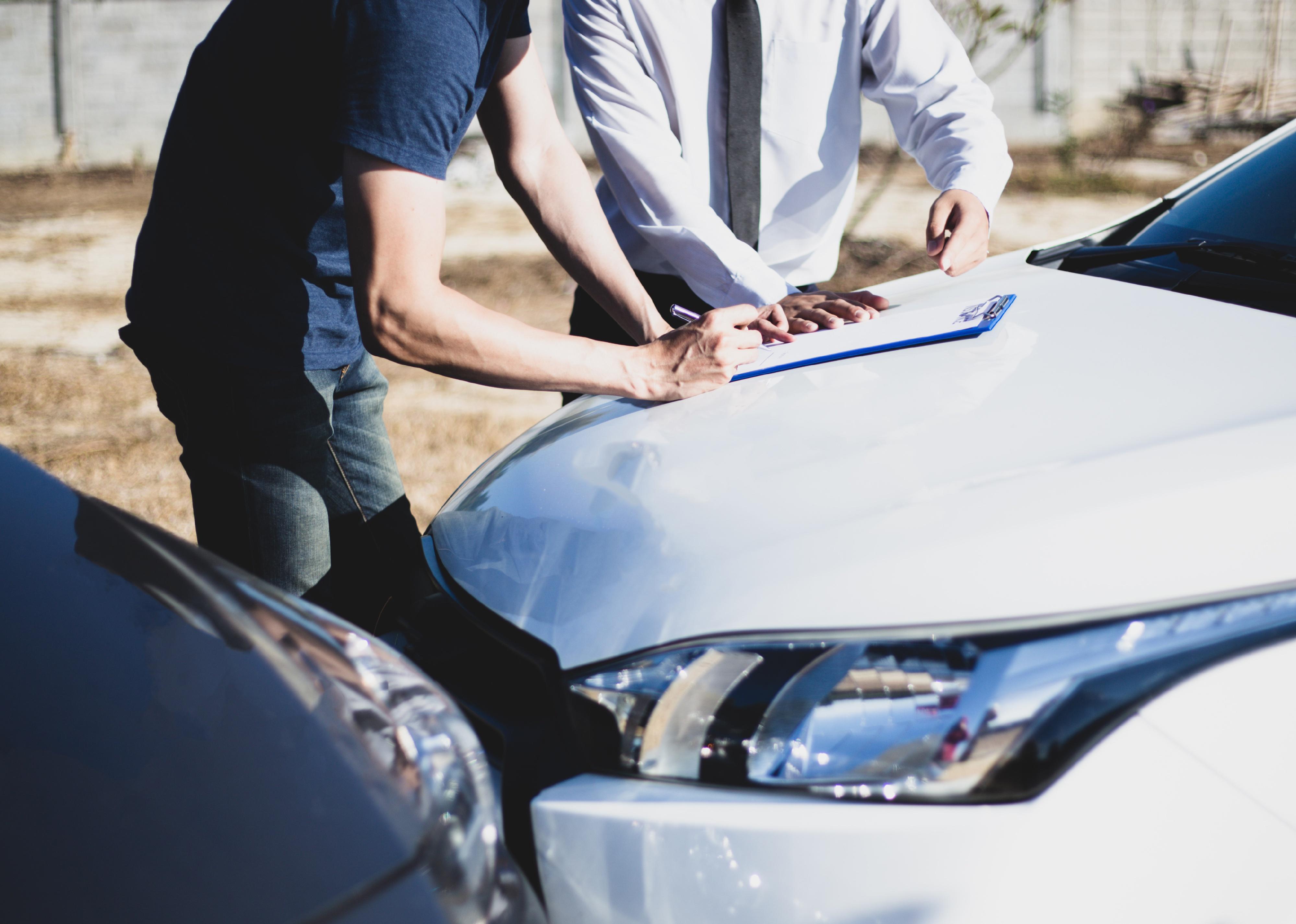 Man and insurance agent look at clipboard over damaged car