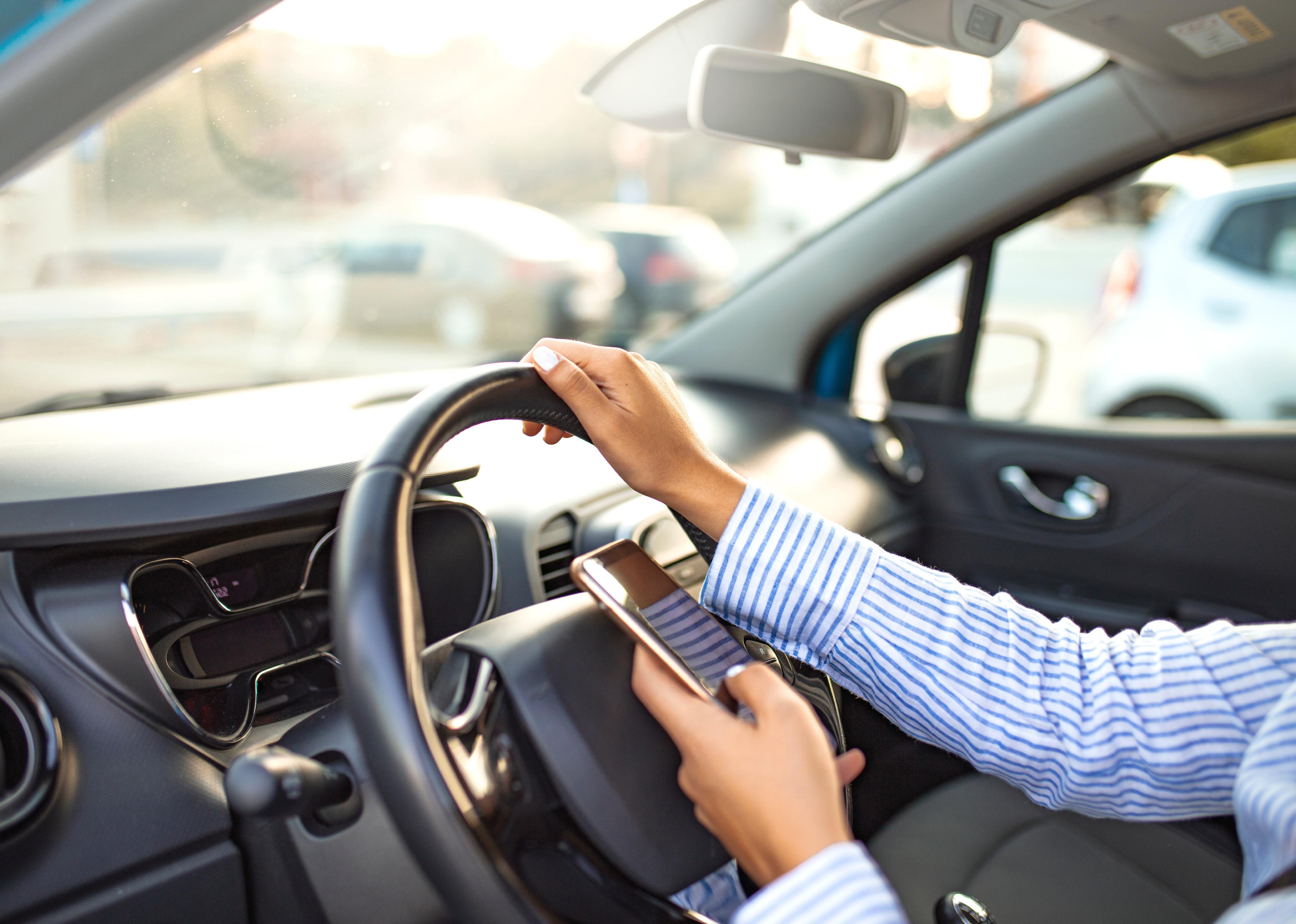 Person using phone while driving behind the wheel.
