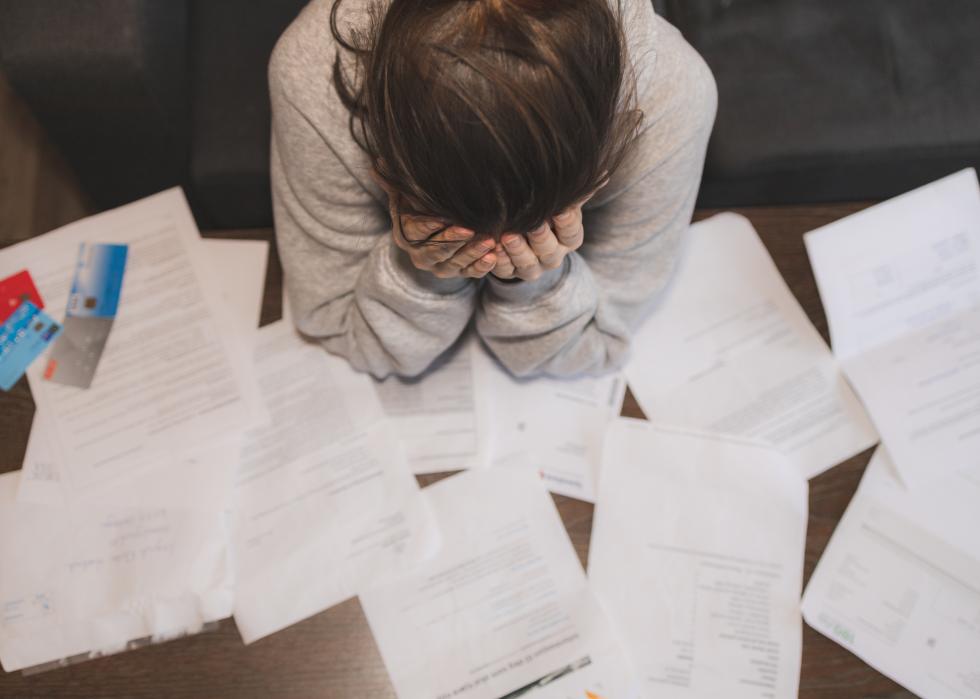 Young woman with face in hands, surrounded by bills