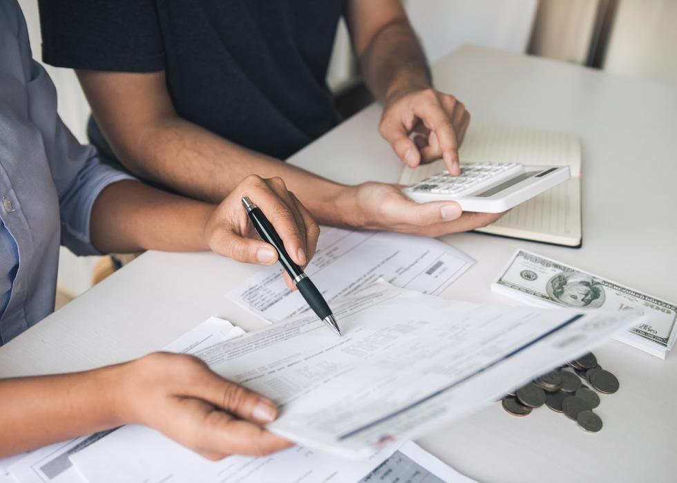 Close-up of two people, one using calculator and the other pointing to paper with pen