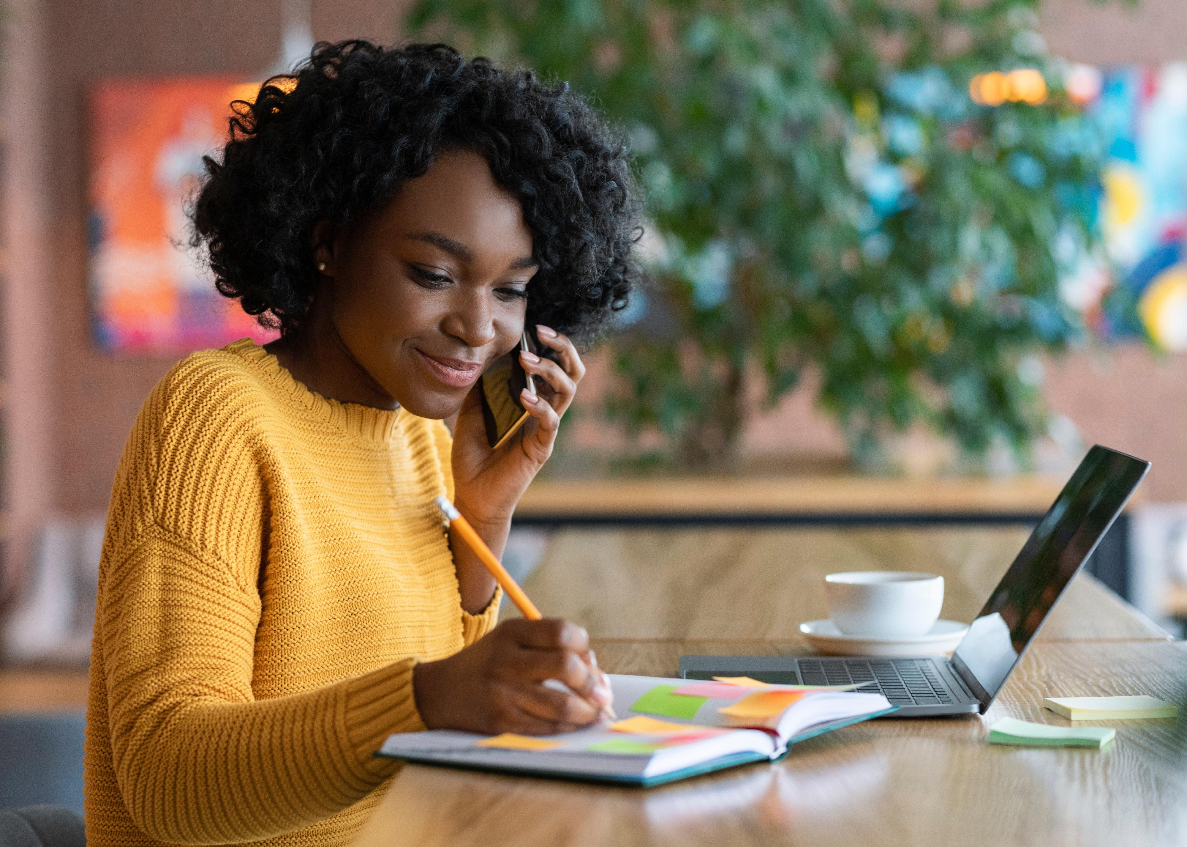 Young woman taking notes while on the phone