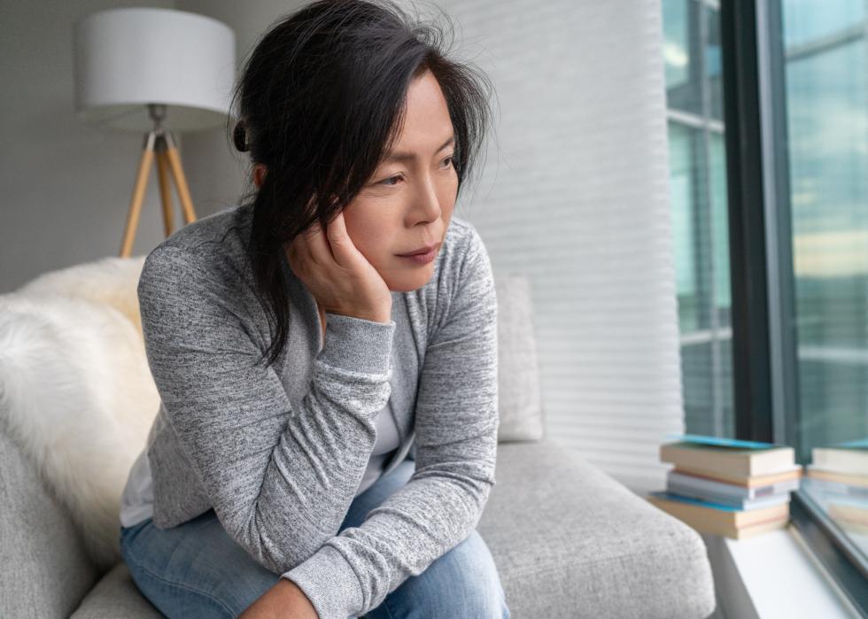 Sad woman looking out window on grey couch 