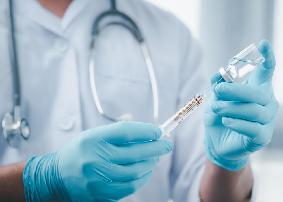 Doctor with gloves using a syring on a vial.