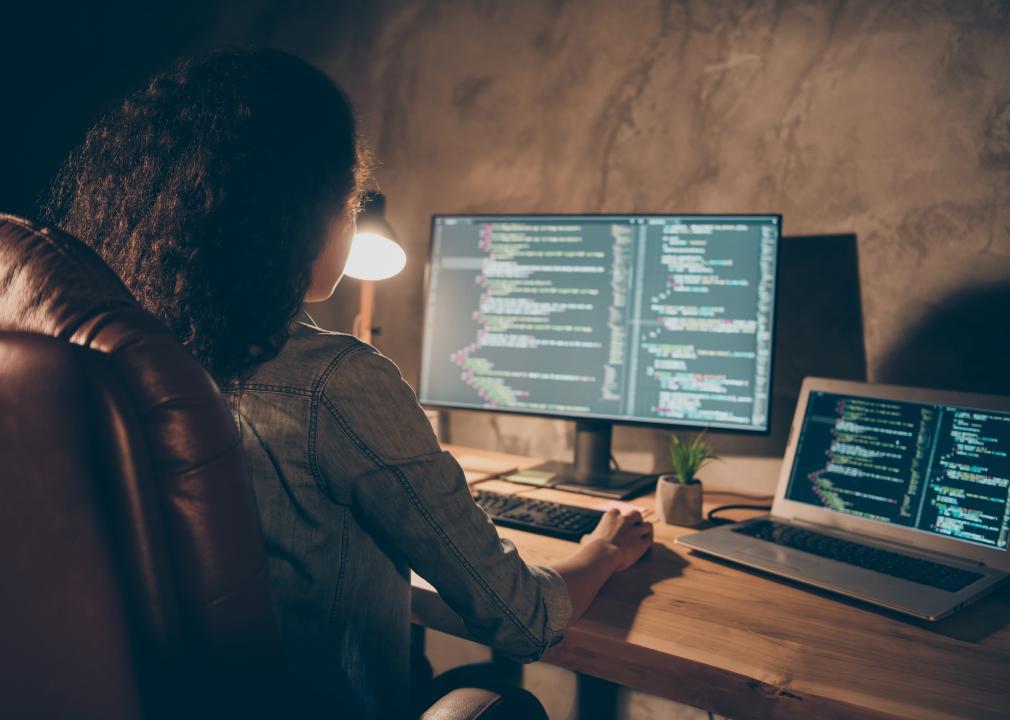Woman software developer working at multiple computers at her desk.