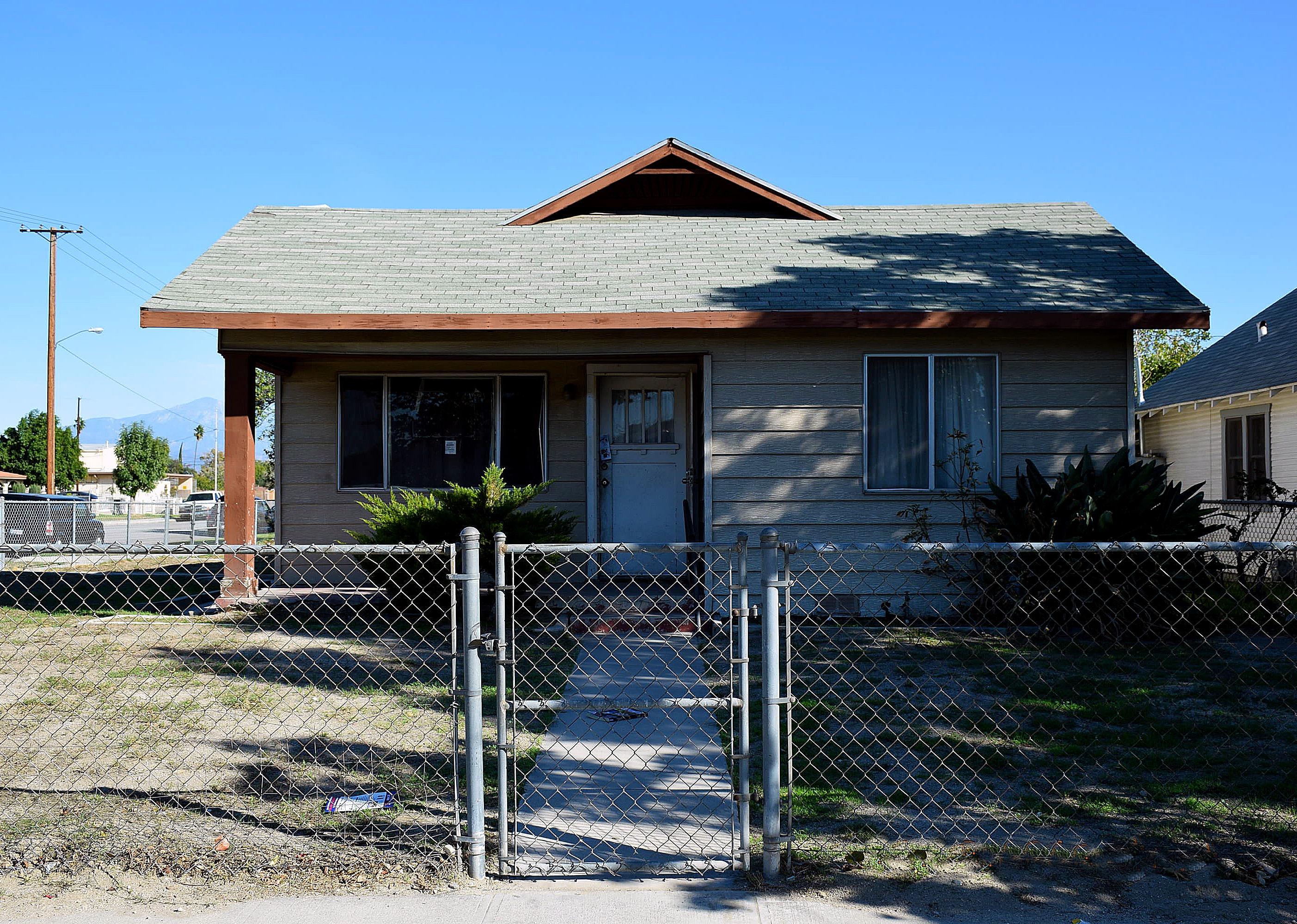 Vacant home from curb behind a chain link fence.