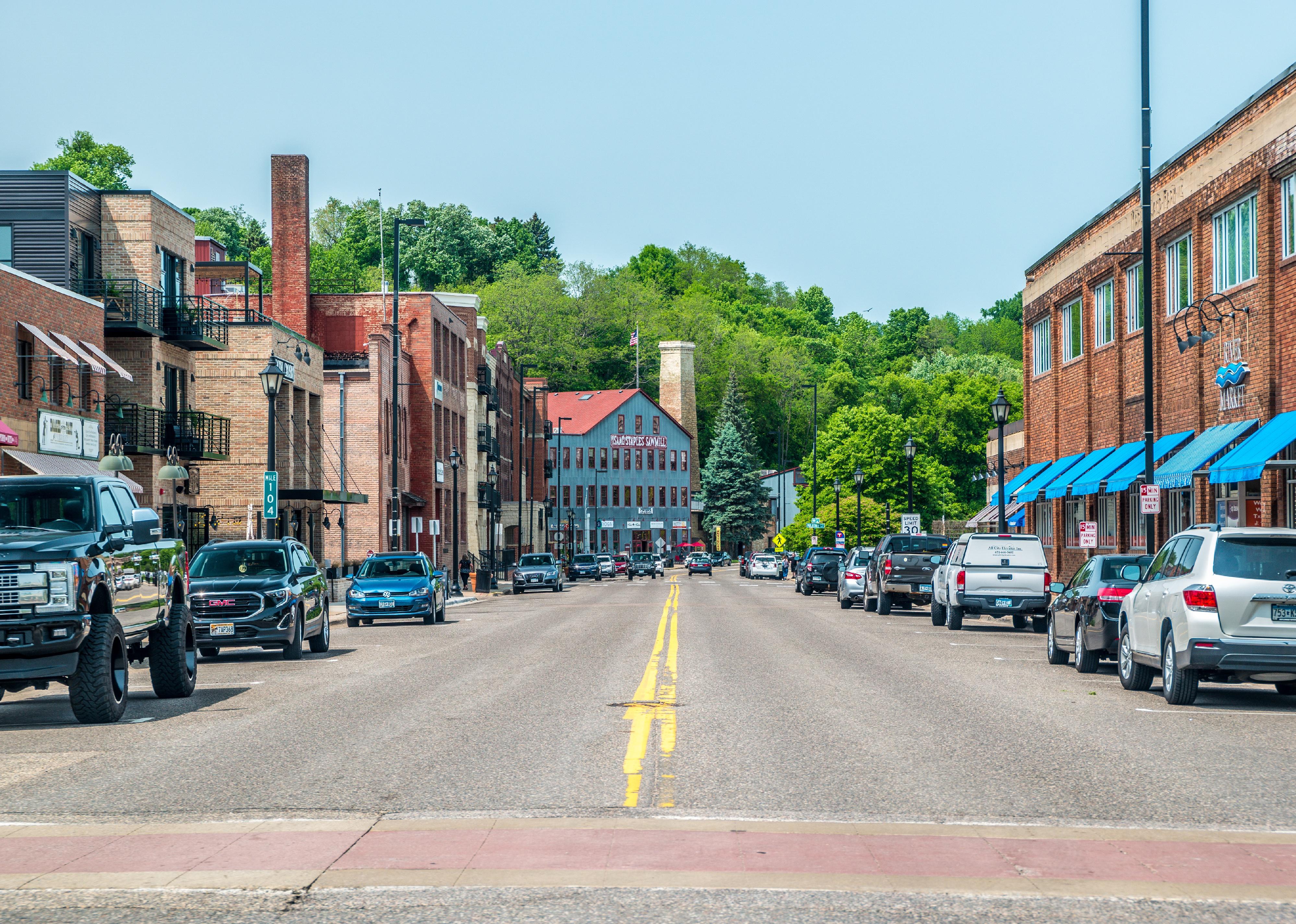 Street view of downtown stores and restaurants and cars parked alongside.