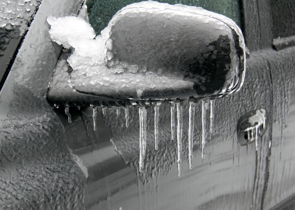 A car side mirror covered in ice with icicles.