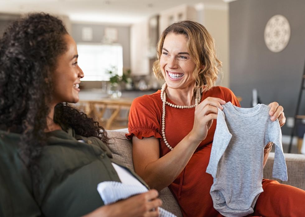 Pregnant woman sitting on couch with woman holding baby clothes