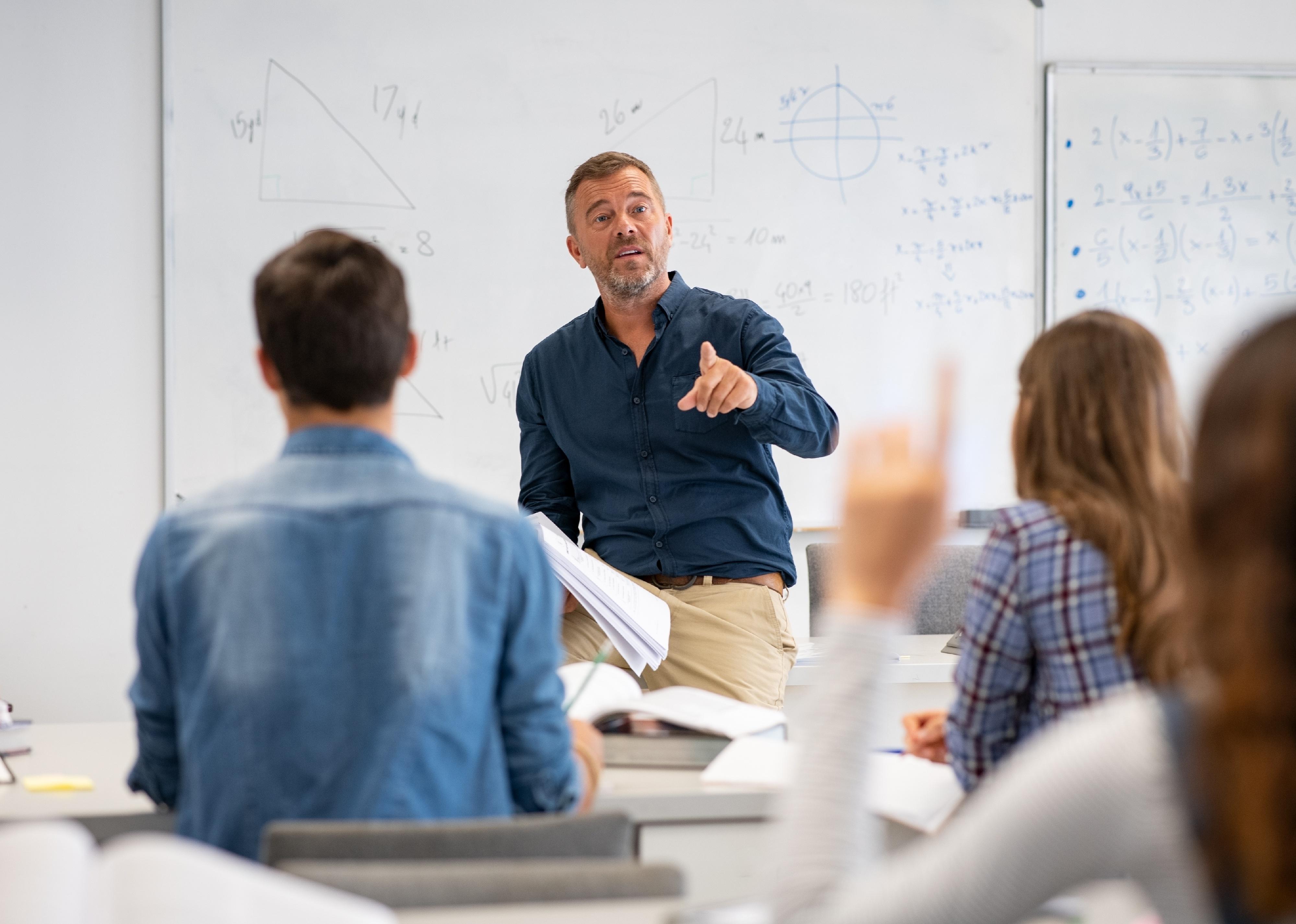 Professor pointing at college student with hand raised in classroom.