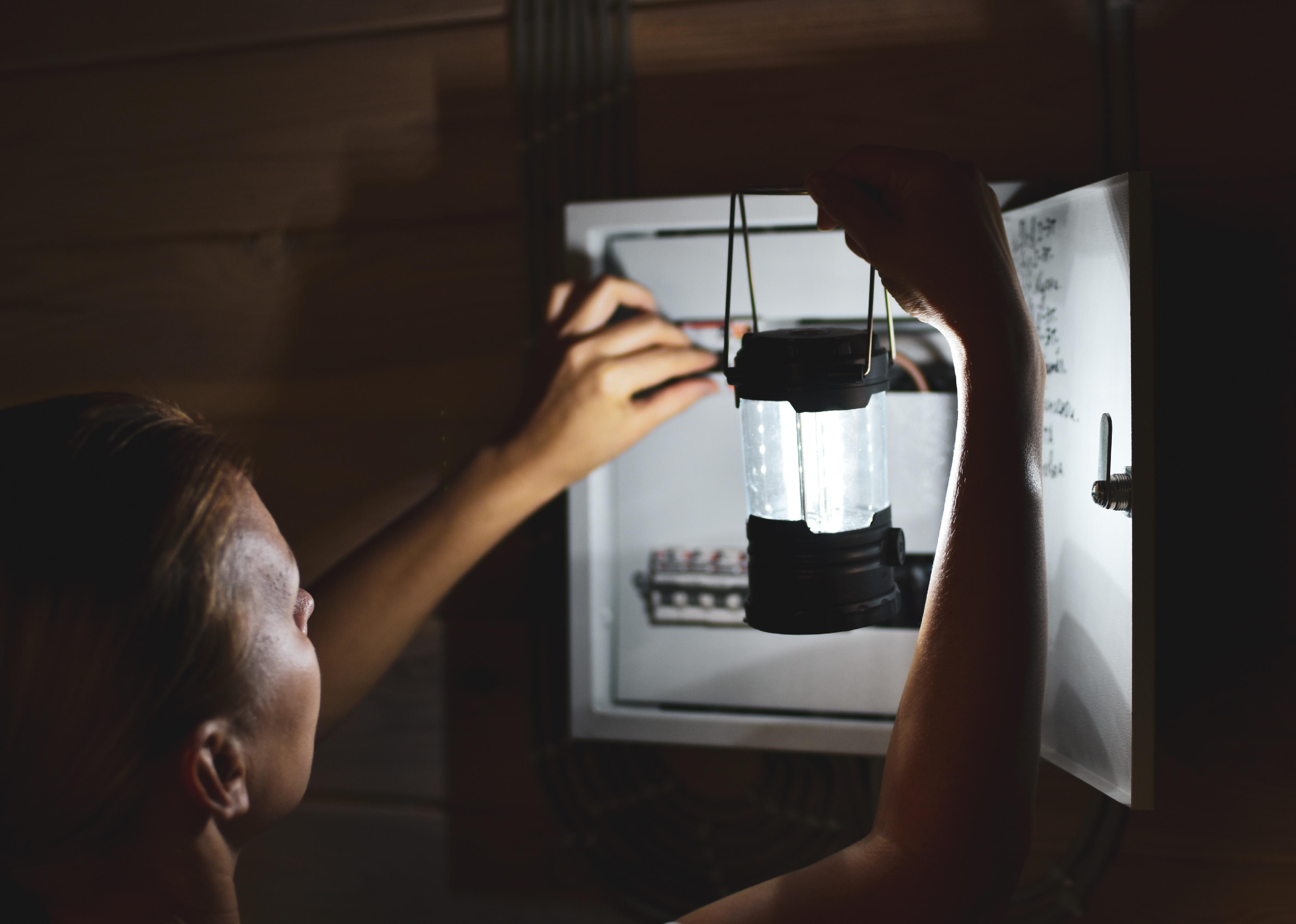 Woman with flashlight looks into distribution board.