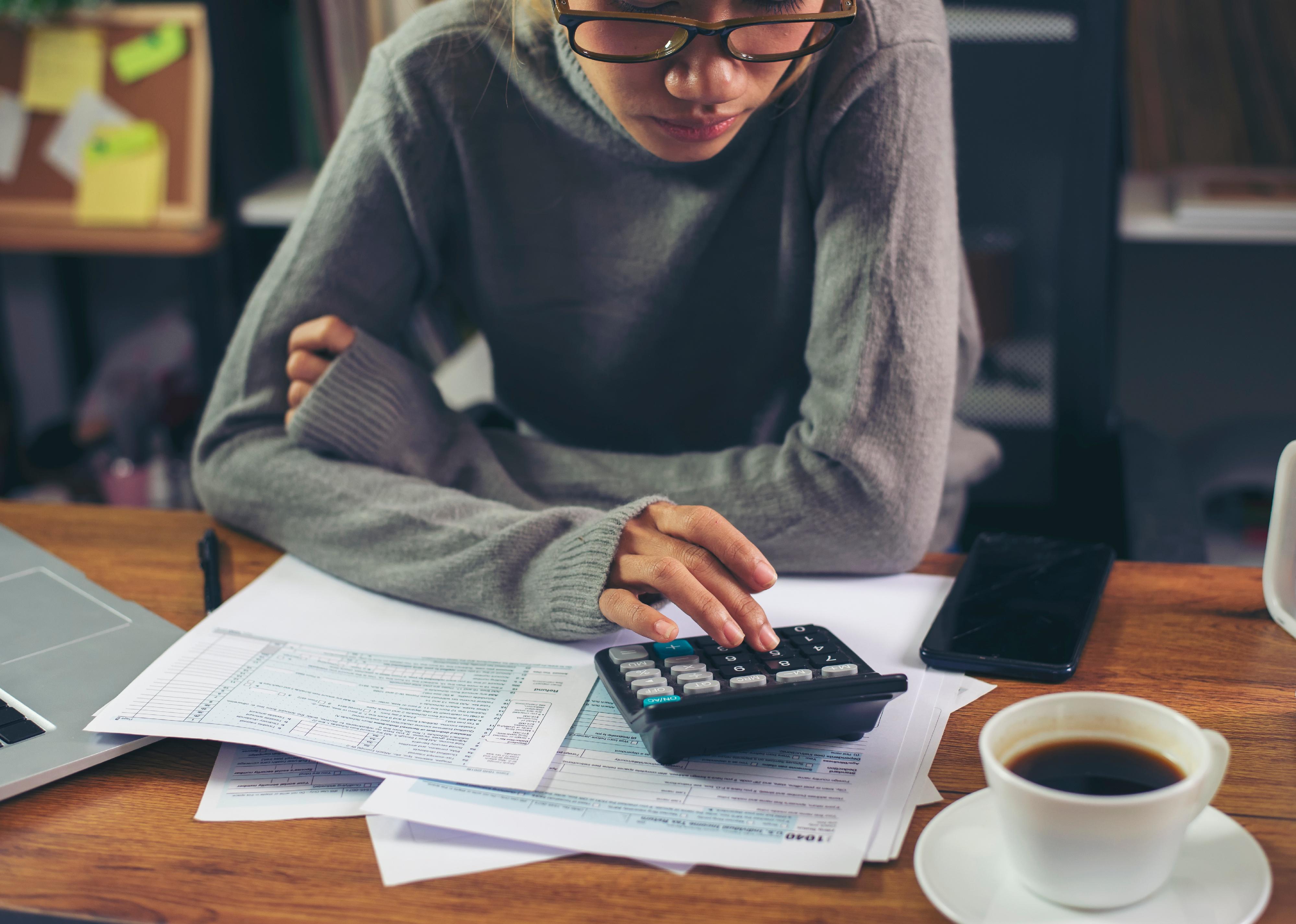Business woman calculating financials and using mobile phone.